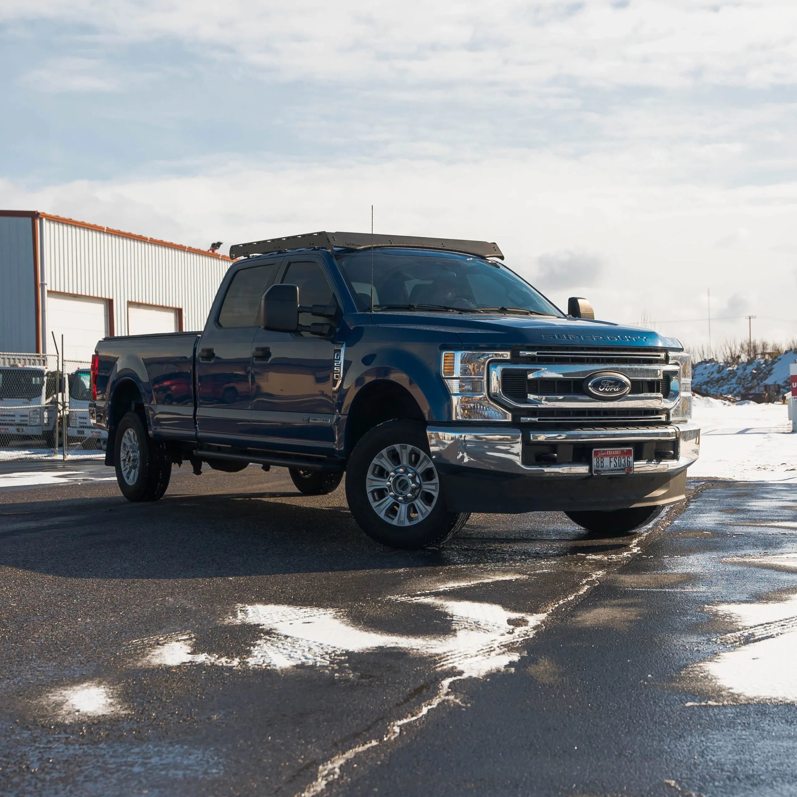 Blue Ford Super Duty truck with roof rack parked outdoors on snowy pavement