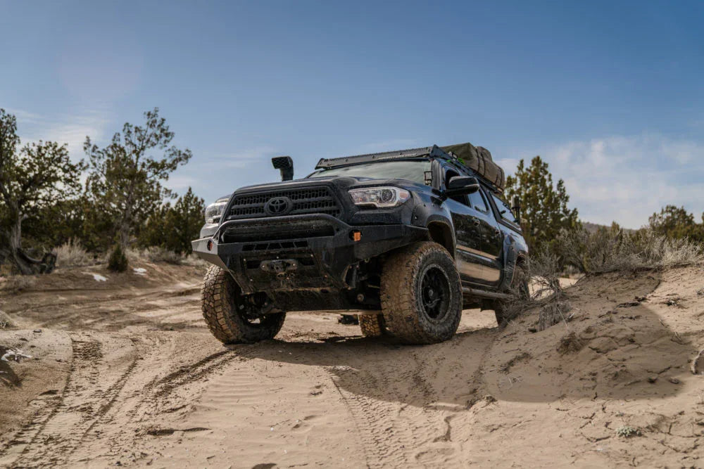 Toyota Tacoma with off-road skids and gear driving on sandy overland trail