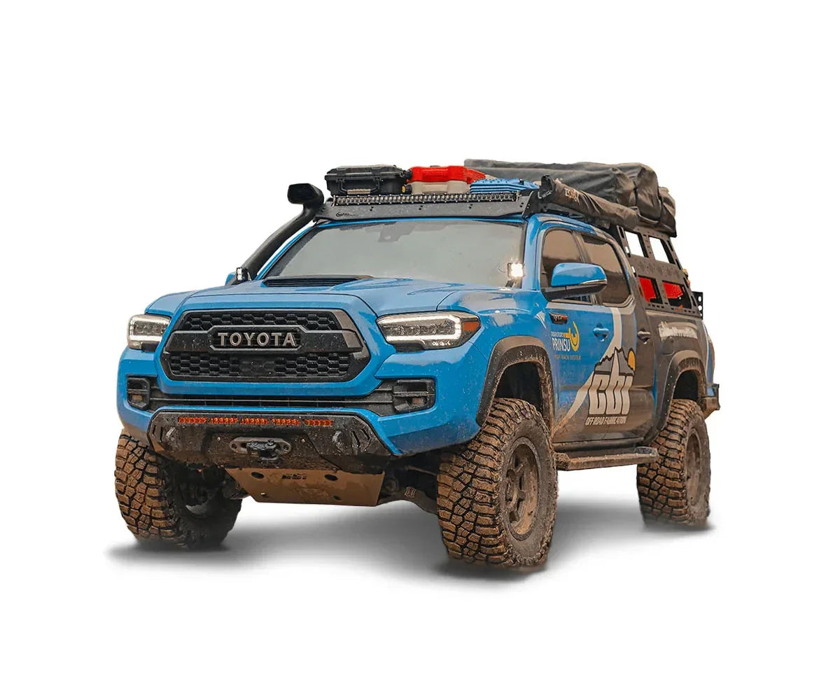 Blue Toyota Tacoma overland truck with off-road tires, roof rack, and camping gear