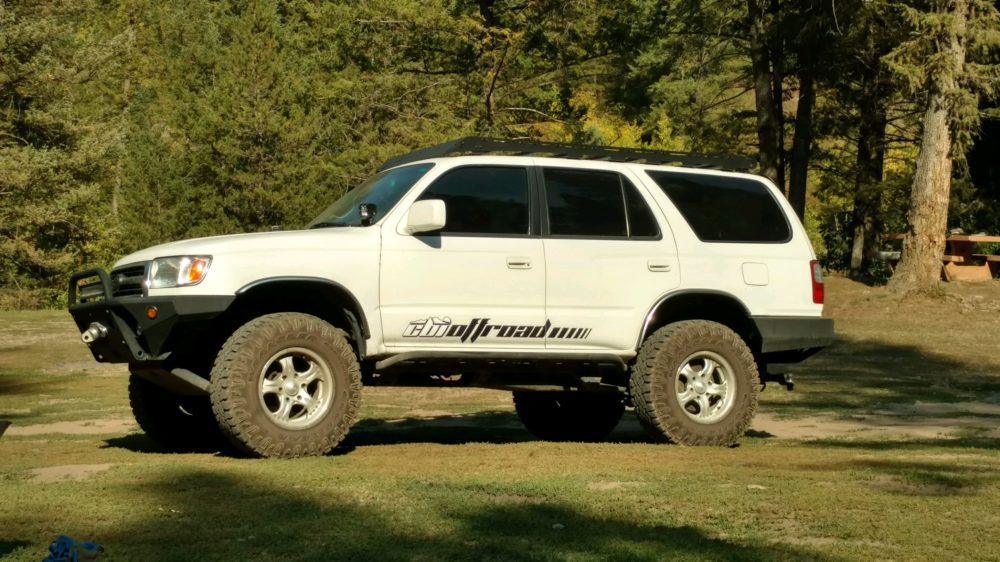 White Toyota 4Runner SUV with off-road tires and roof rack parked outdoors