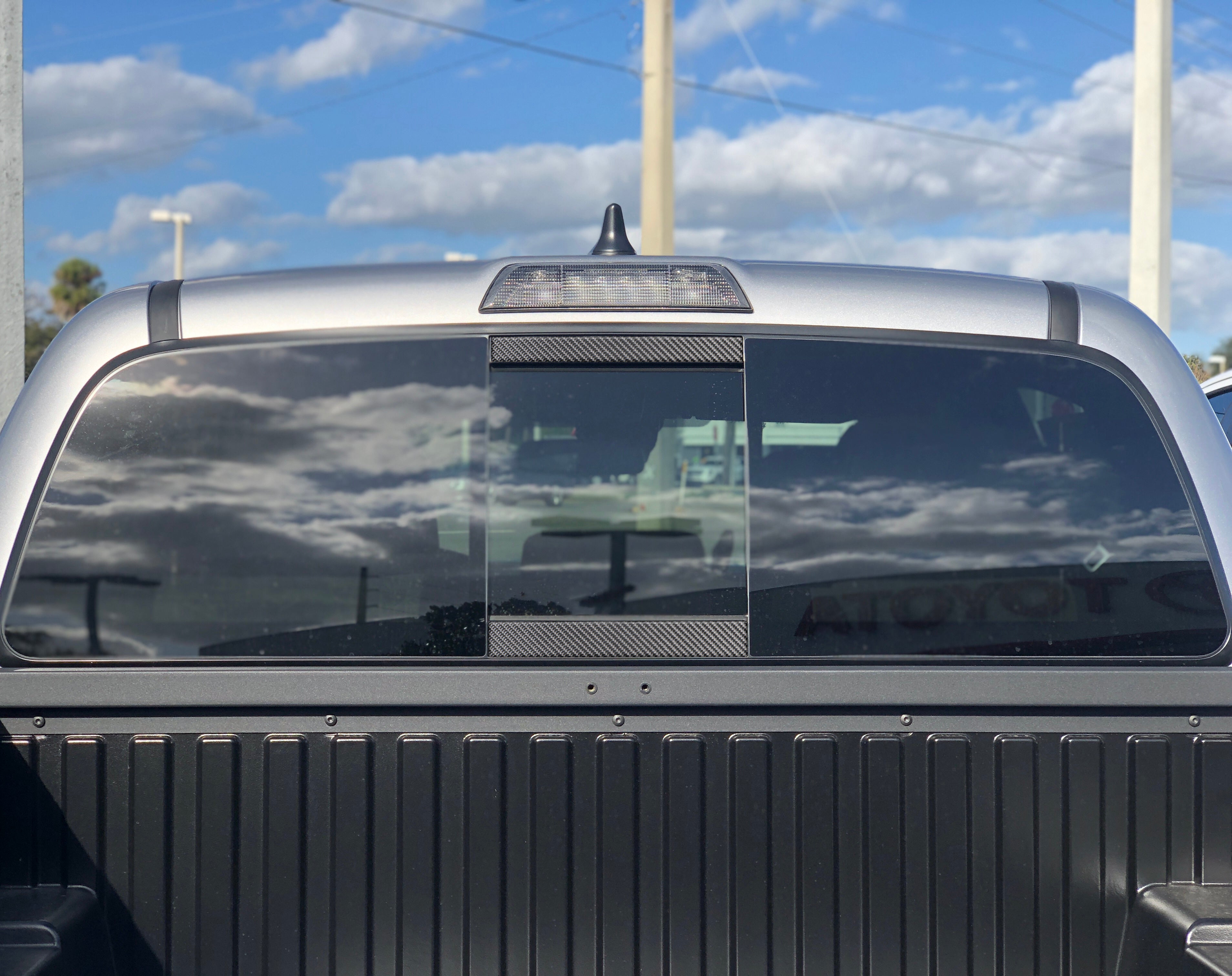Toyota Tacoma rear window with carbon fiber panel under blue sky reflection