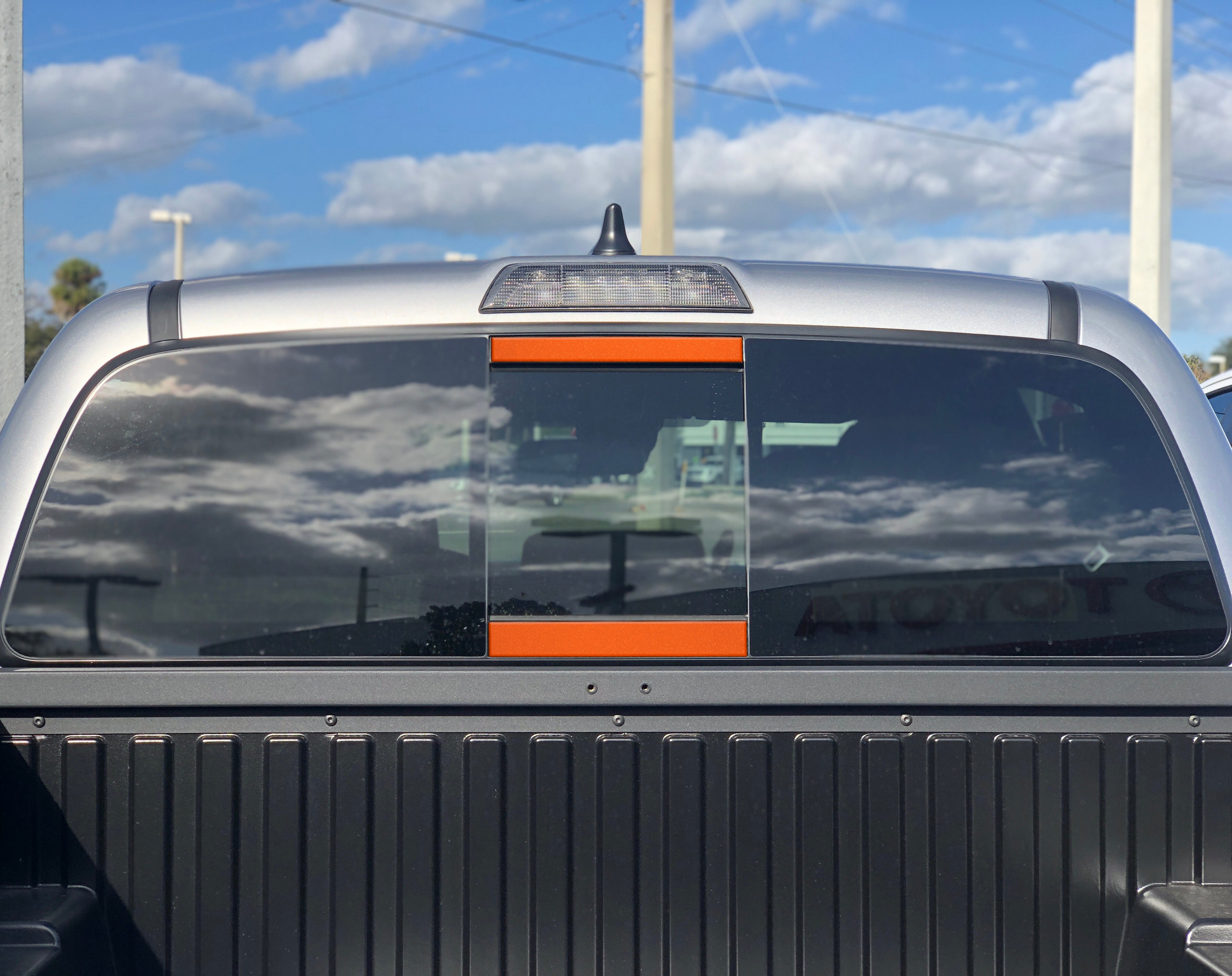 Toyota Tacoma rear cab window with orange accent panels and outdoor reflection
