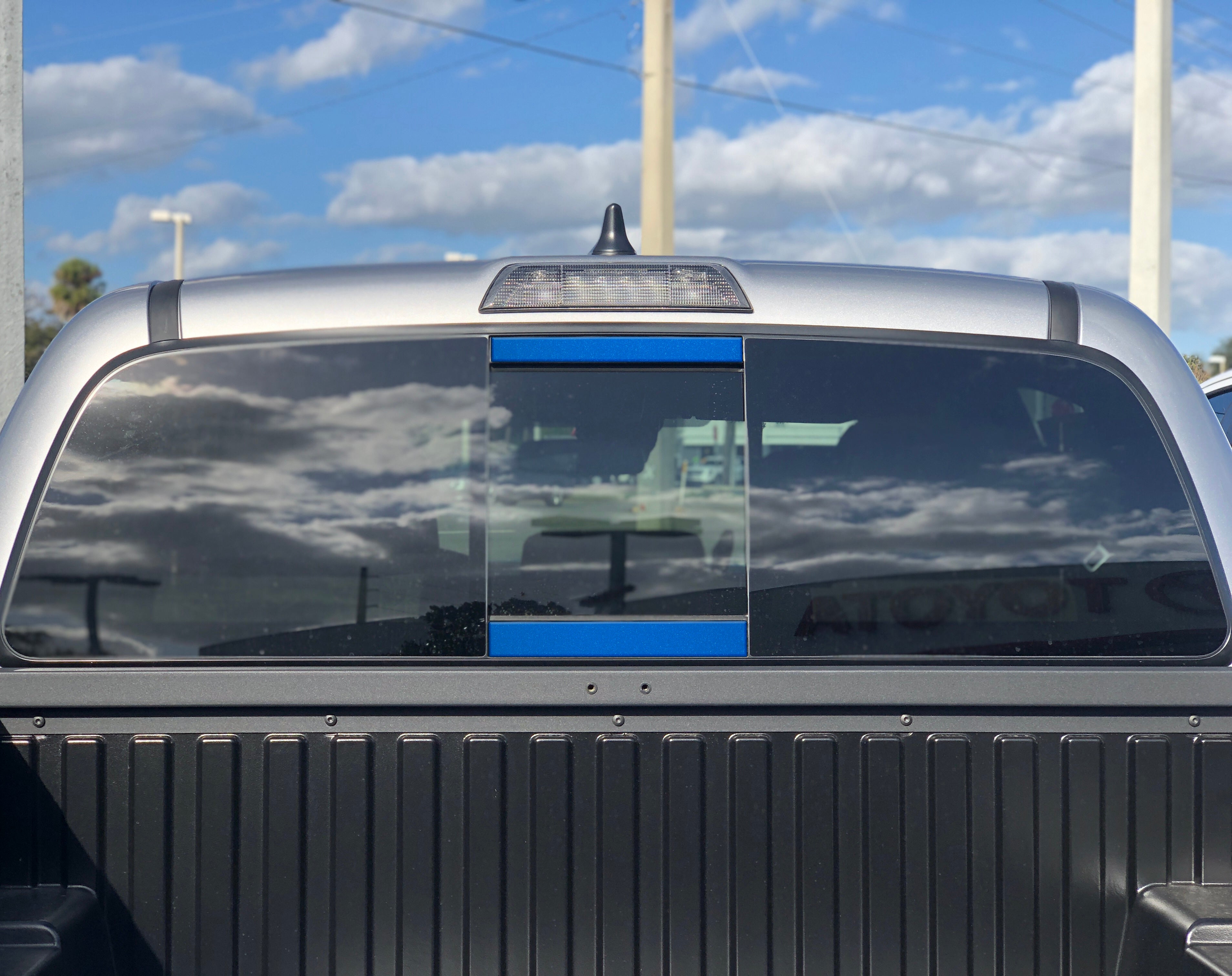 Toyota Tacoma rear window with blue trim accent, clear sky reflection, pickup truck bed