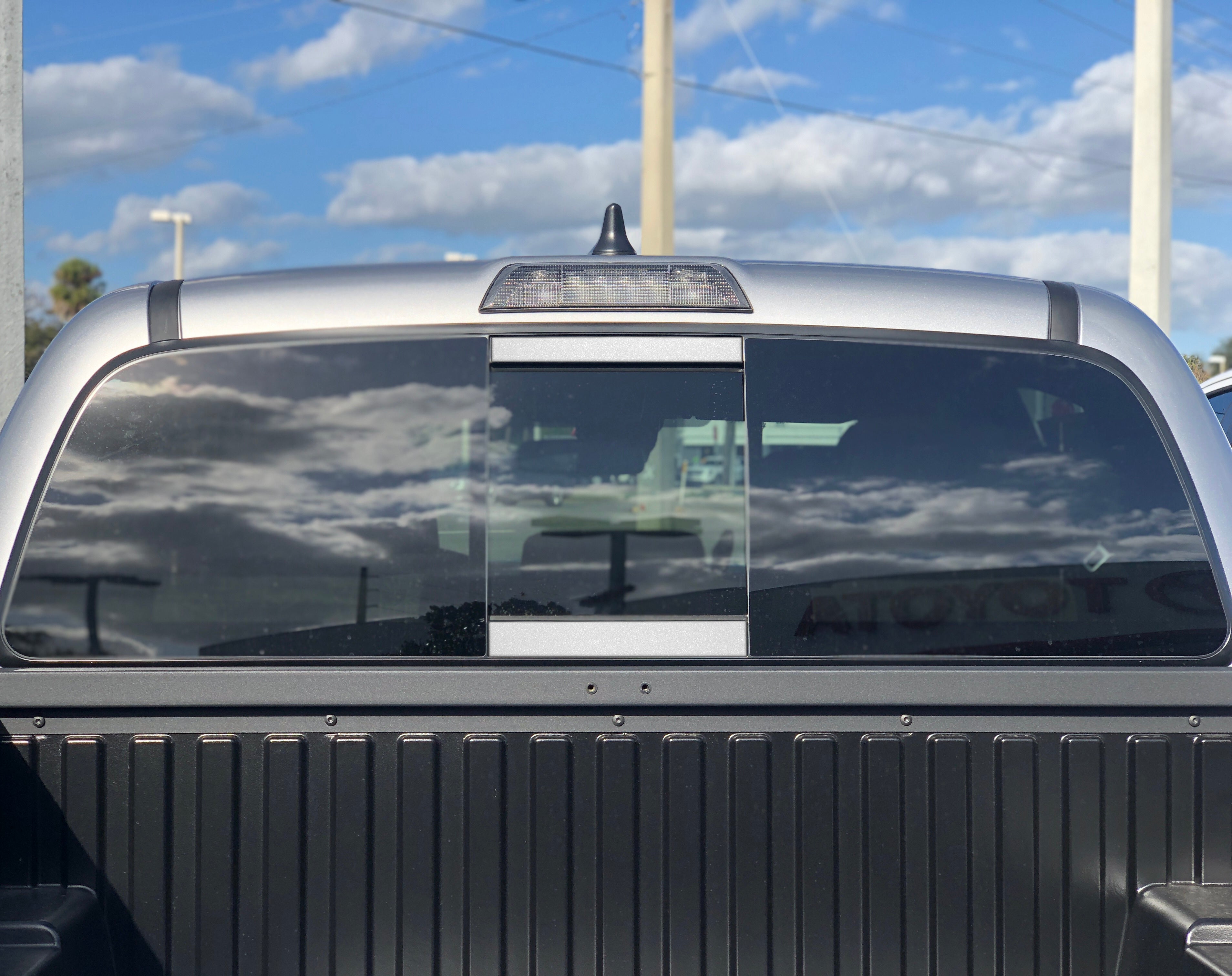 Close-up of a Toyota Tacoma rear window and truck bed under blue sky, ideal for overlanding gear.