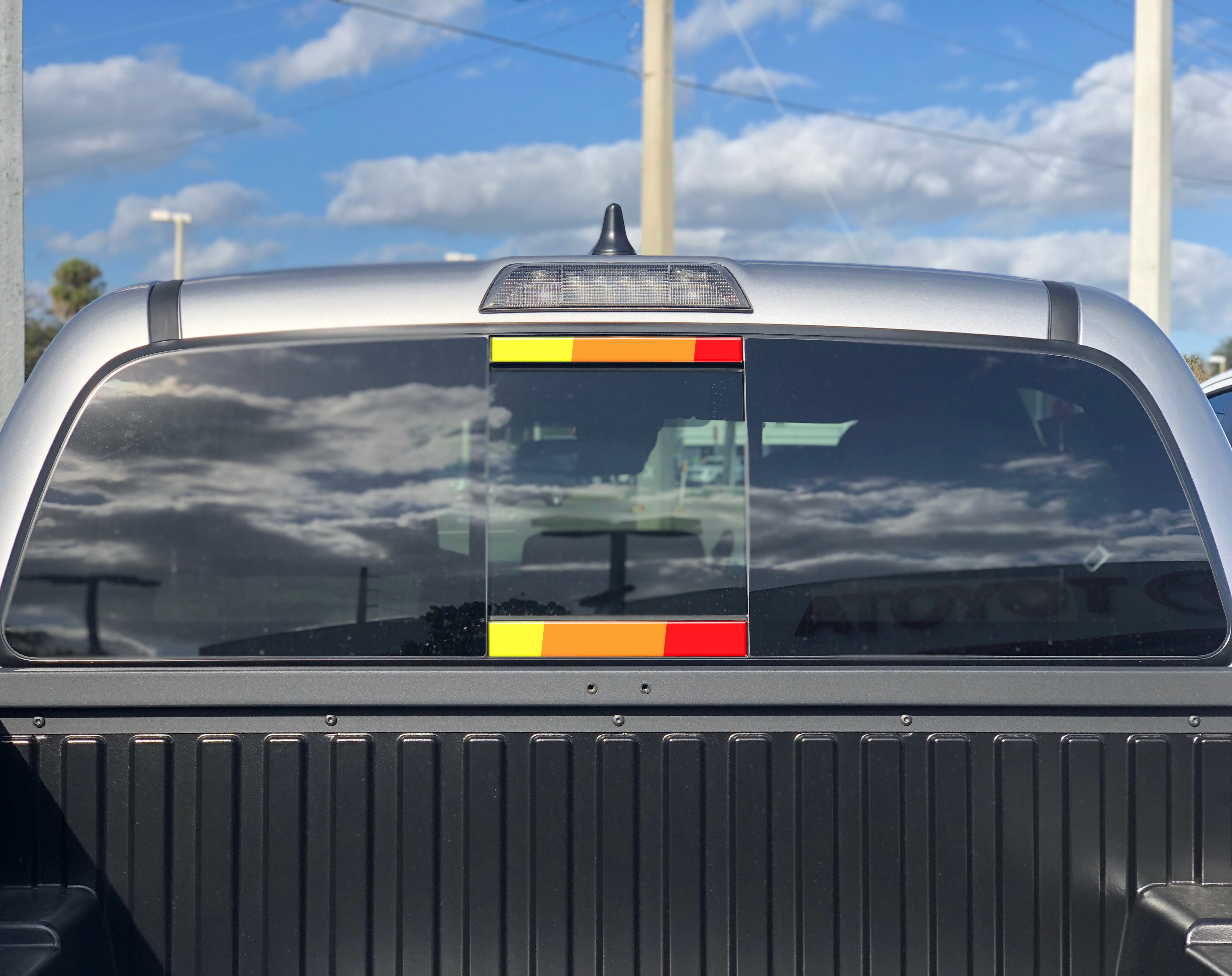 Toyota Tacoma rear window with red, orange, and yellow retro stripe decal for overlanding