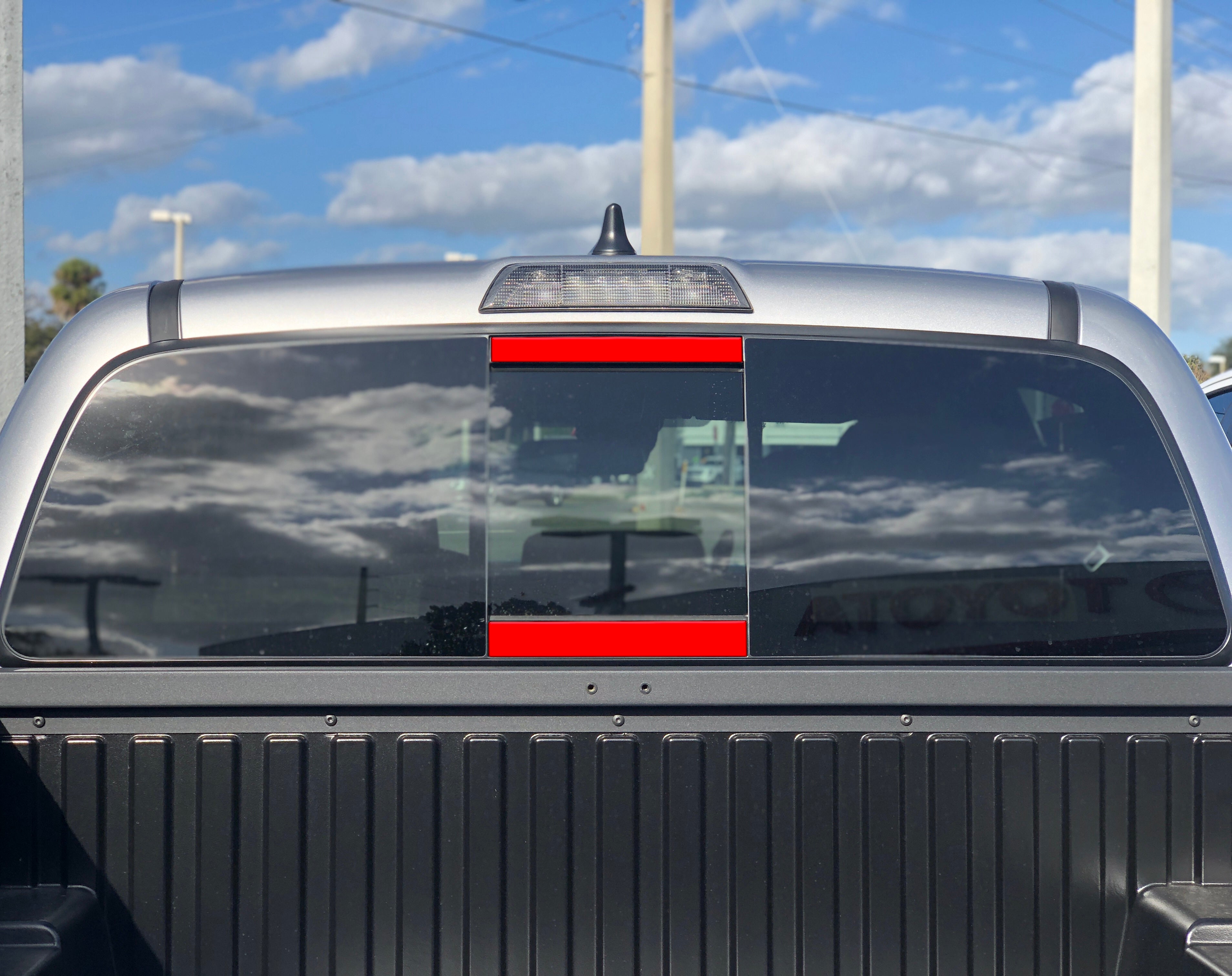 Red overlay window decal on rear window of a Toyota Tacoma truck under blue sky