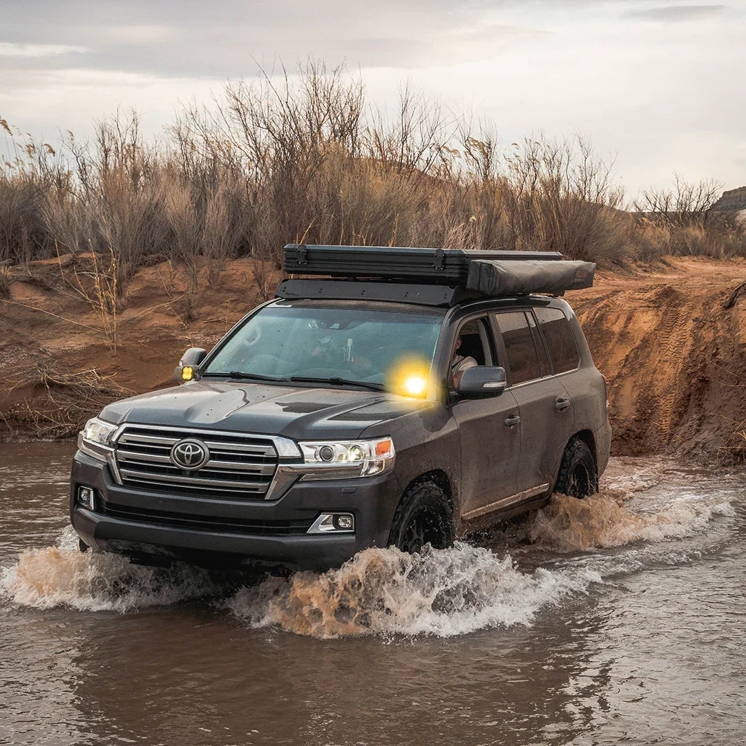 Toyota 200 Series Land Cruiser with ditch light brackets and camping gear off-roading through water
