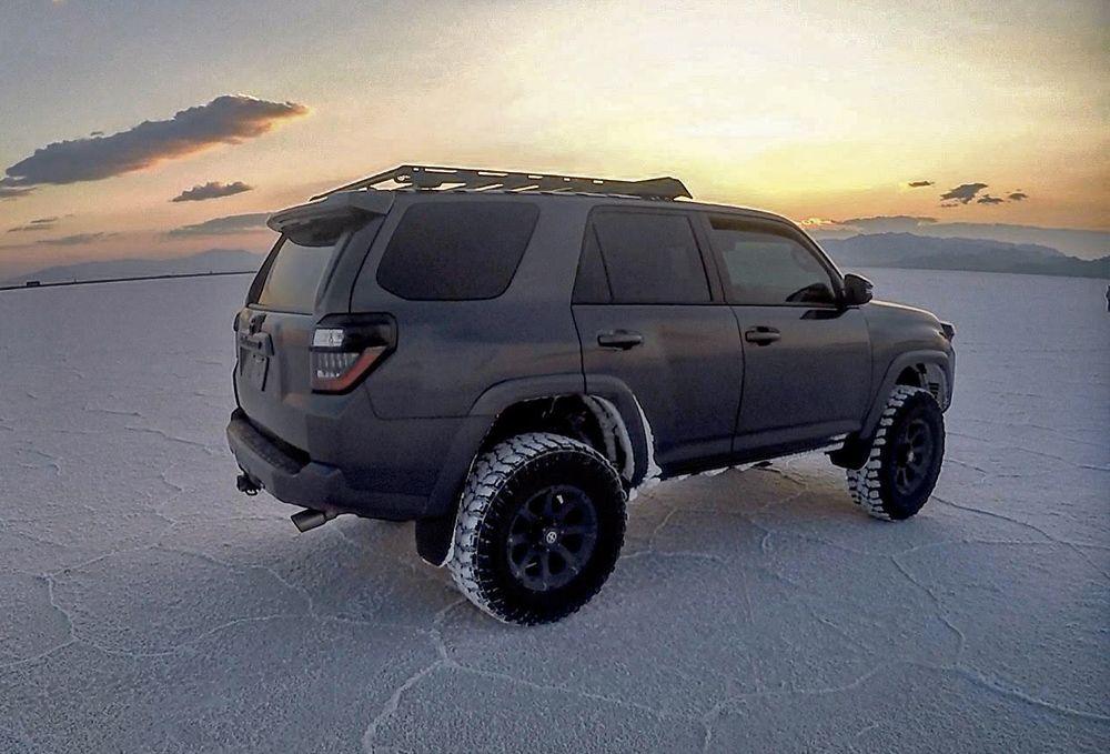 Toyota 4Runner with roof rack and off-road tires parked on salt flats at sunset