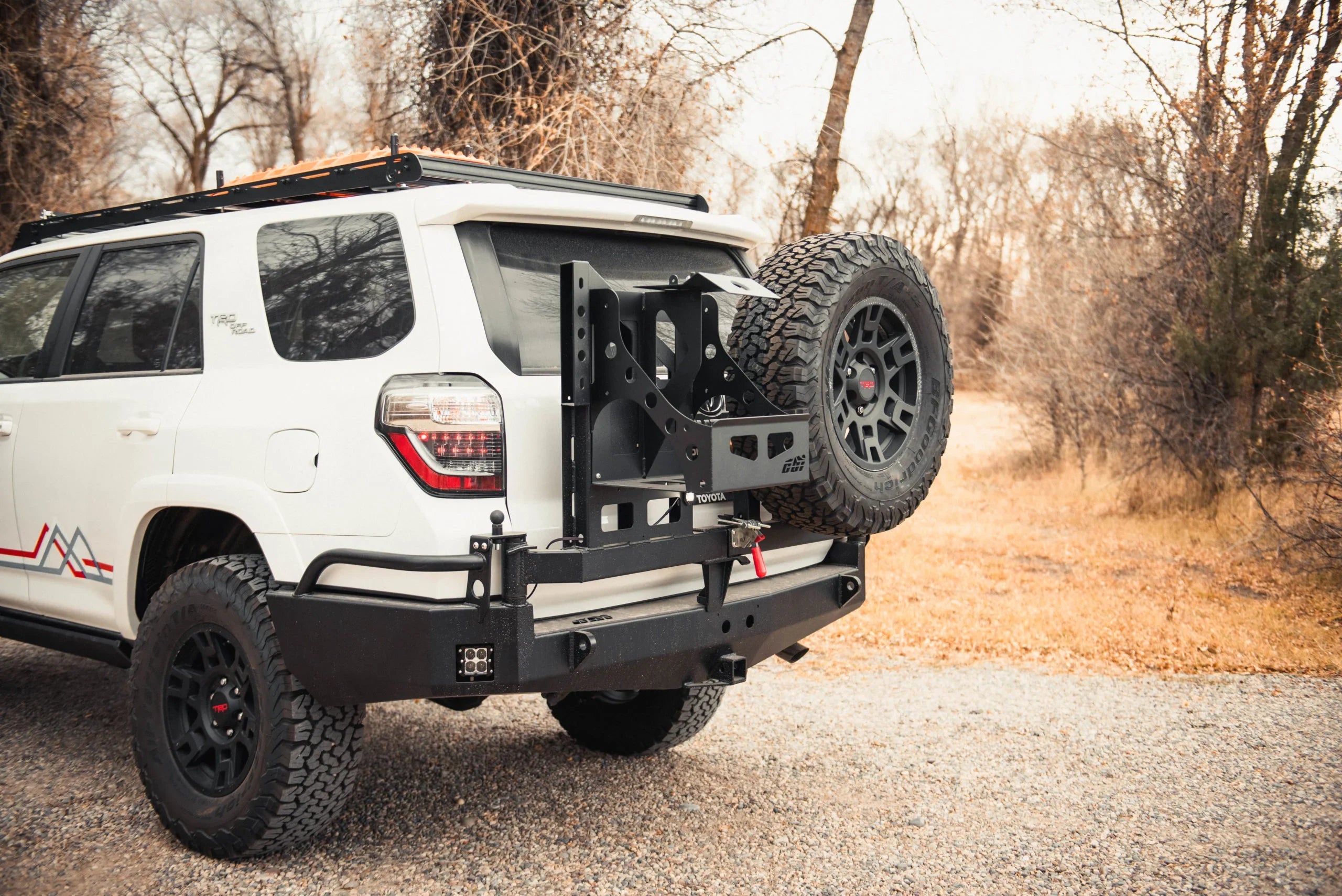 Toyota 4Runner with swing arm rear bumper and spare tire, parked outdoors on gravel
