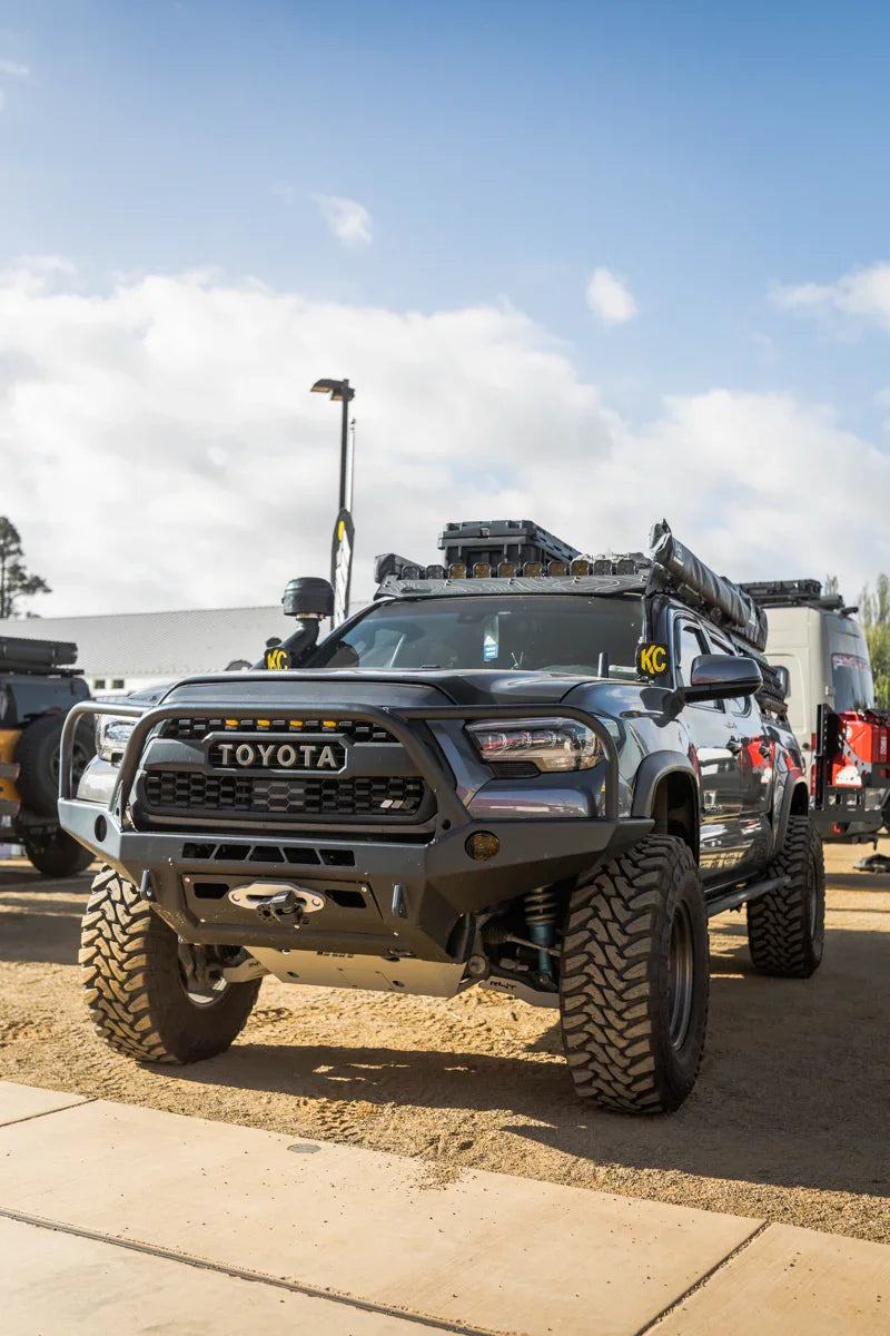 Toyota Tacoma with off-road tires, roof rack and camping gear at outdoor adventure event