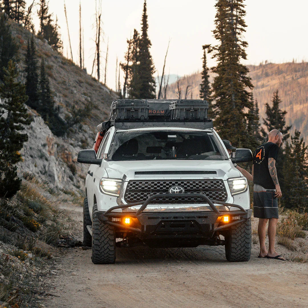 Toyota Tundra with ditch light brackets and roof gear driving on a rugged forest trail