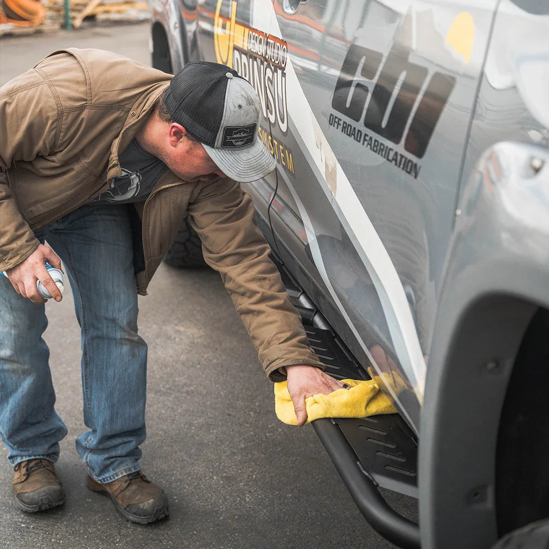 Man cleaning black overland rock sliders on Toyota Tundra truck outdoors