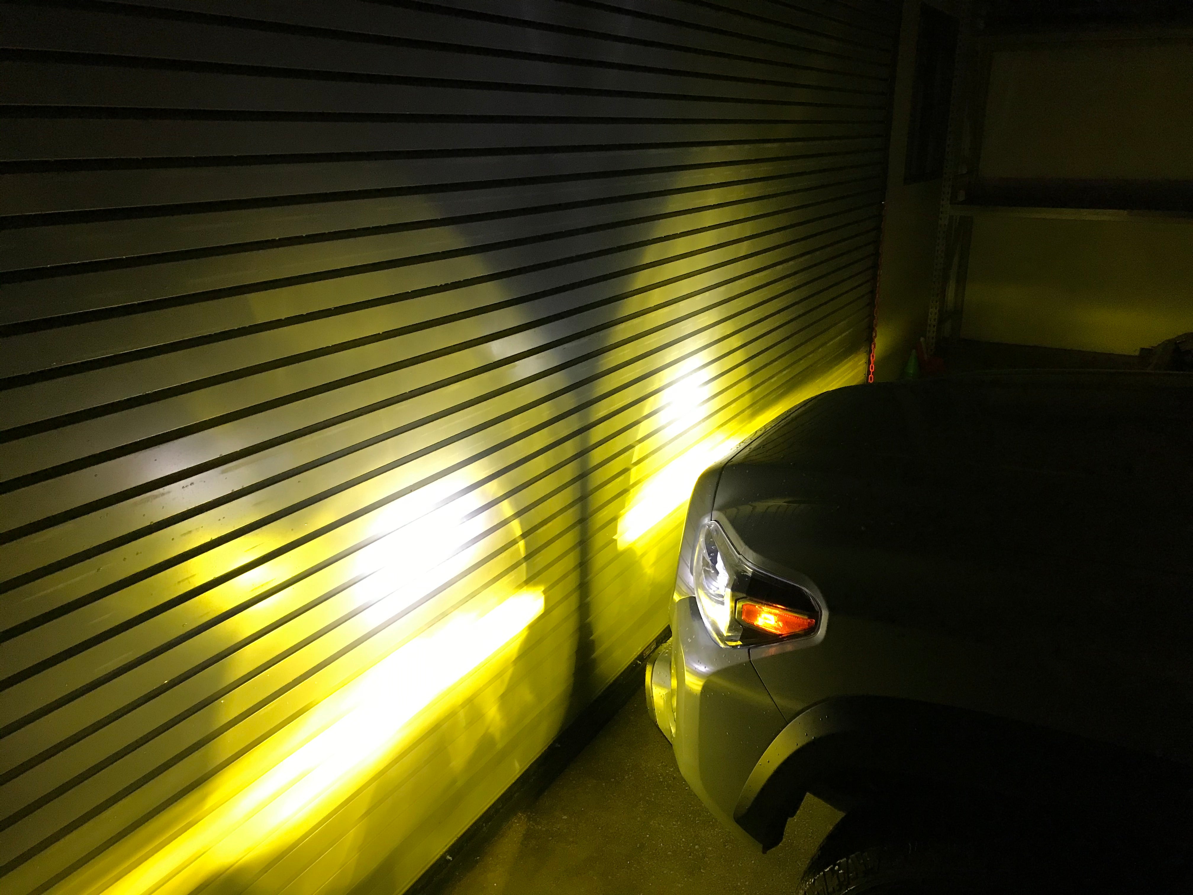 Toyota SUV with tri-color fog lights illuminating a garage wall, yellow and white beam pattern