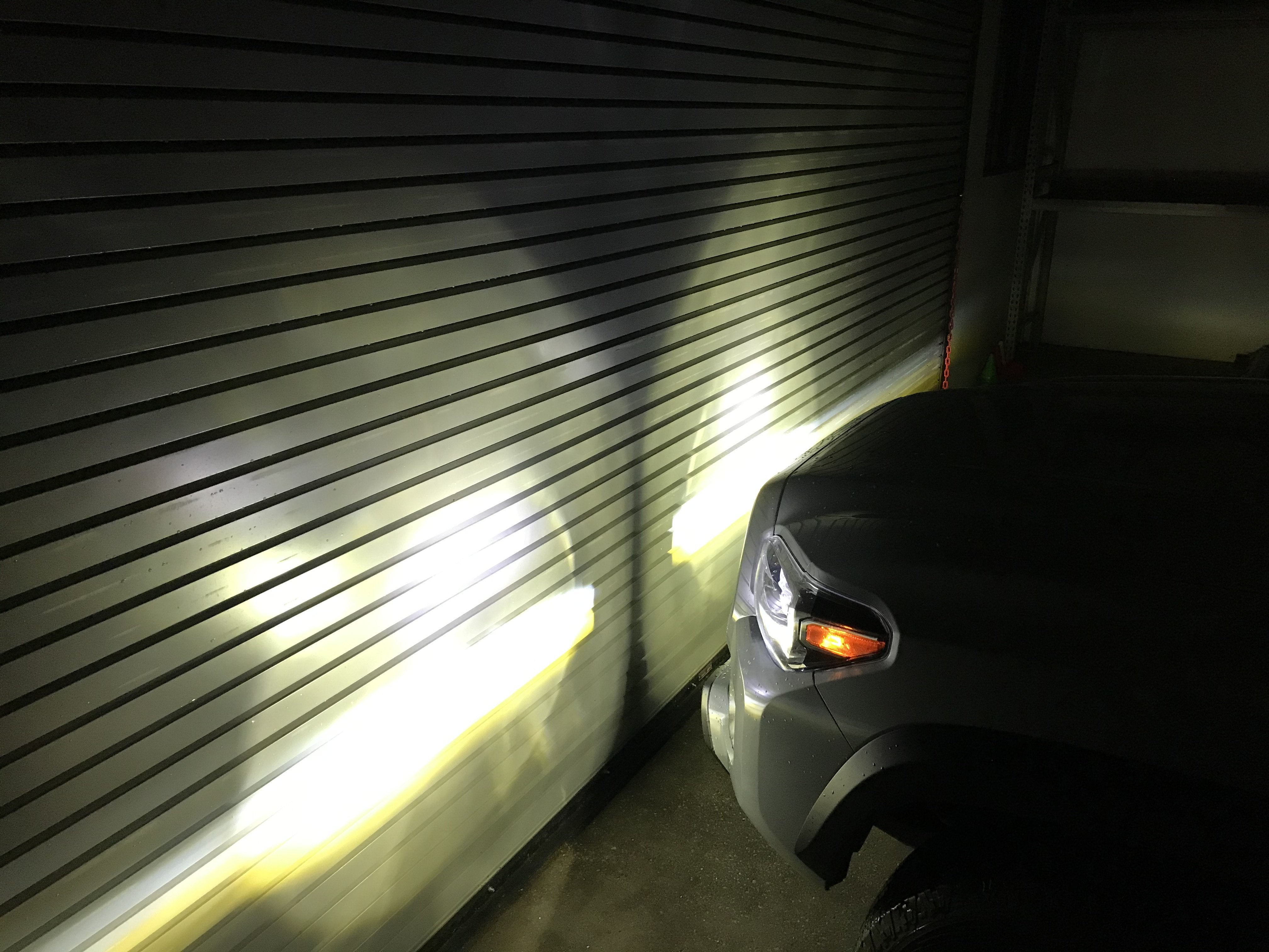Toyota SUV with tri-color fog lights projecting beams onto a garage door