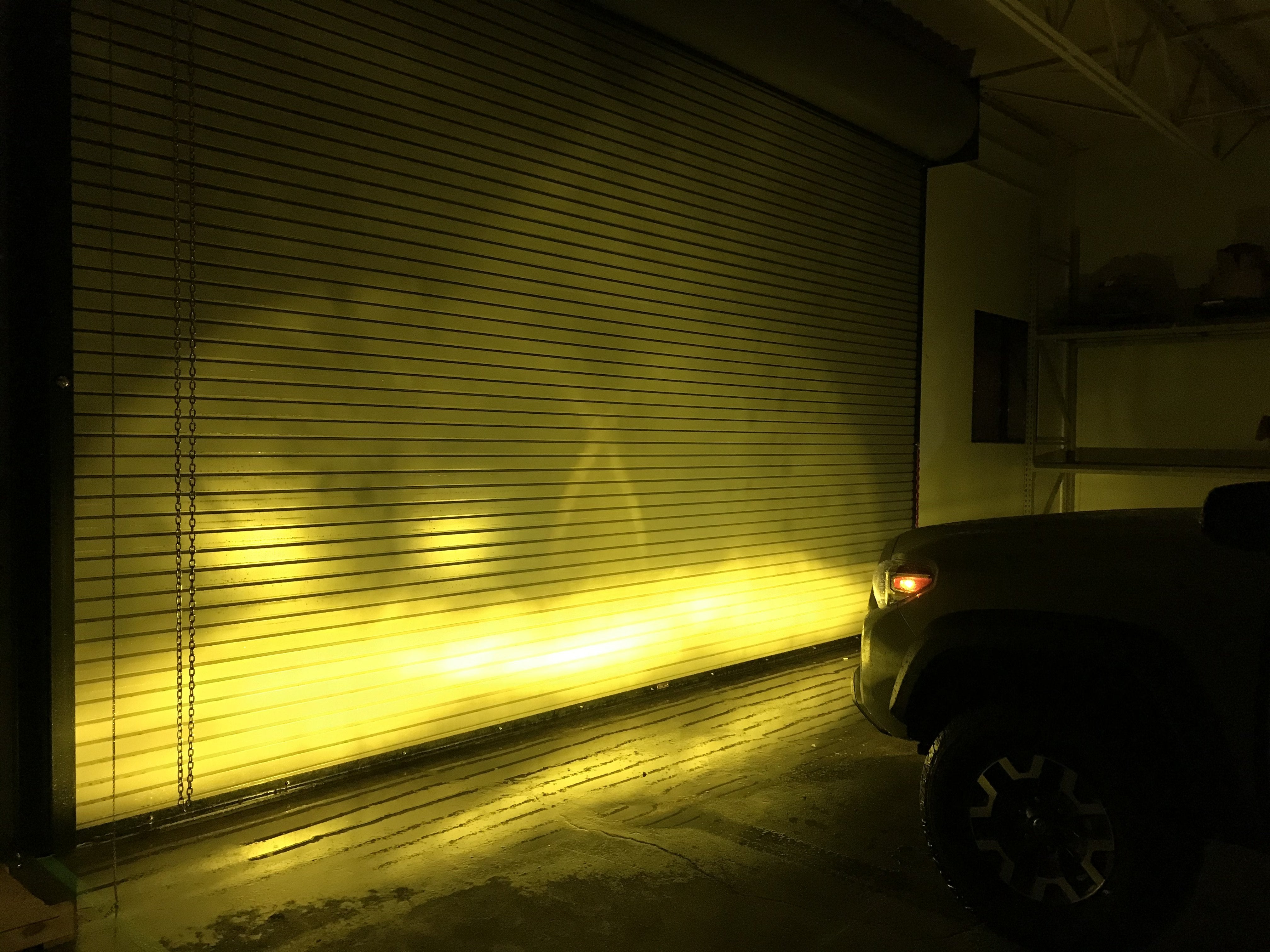 Toyota truck emitting bright yellow fog light beam against a garage door indoors