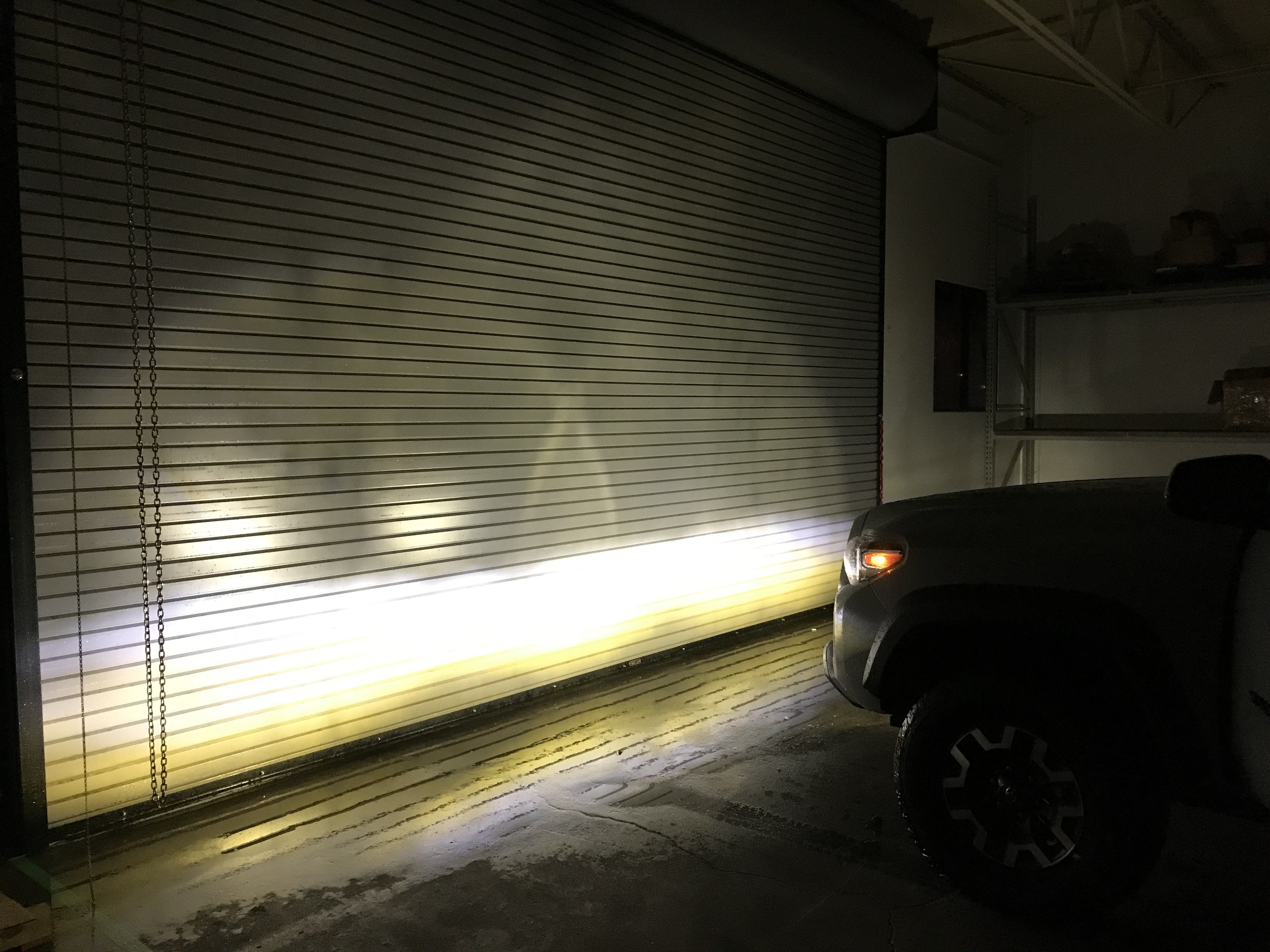 Toyota truck projecting tri-color fog light beam onto garage door in dark warehouse