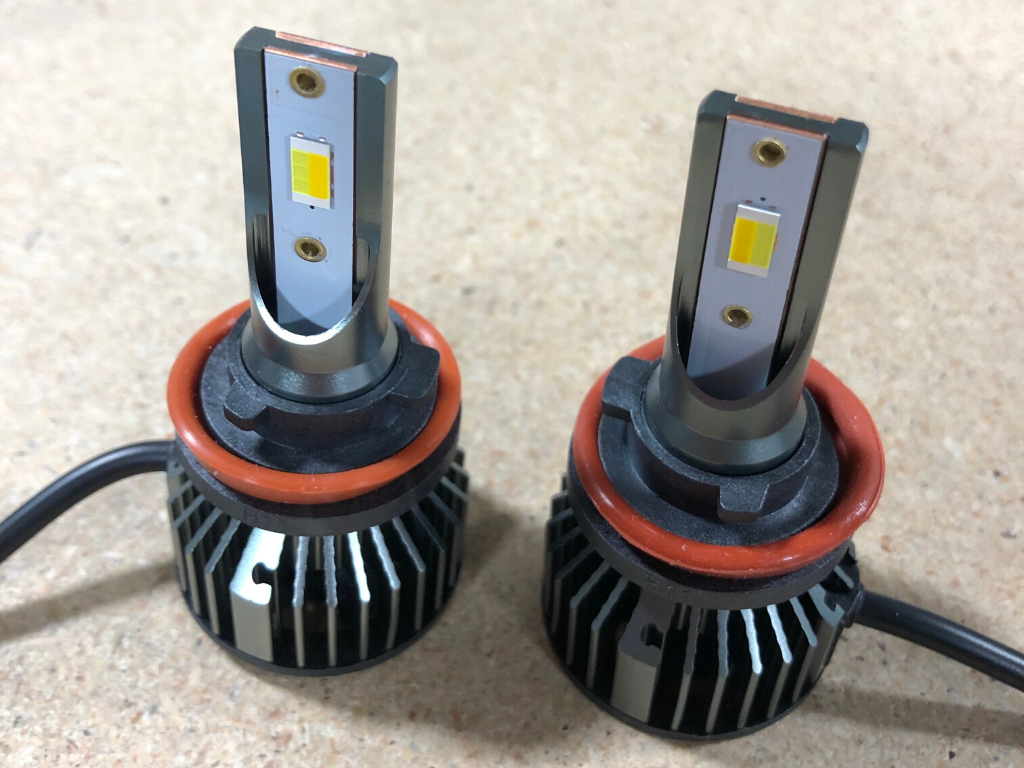 Pair of tri-color LED fog light bulbs for off-road vehicles on a wood surface