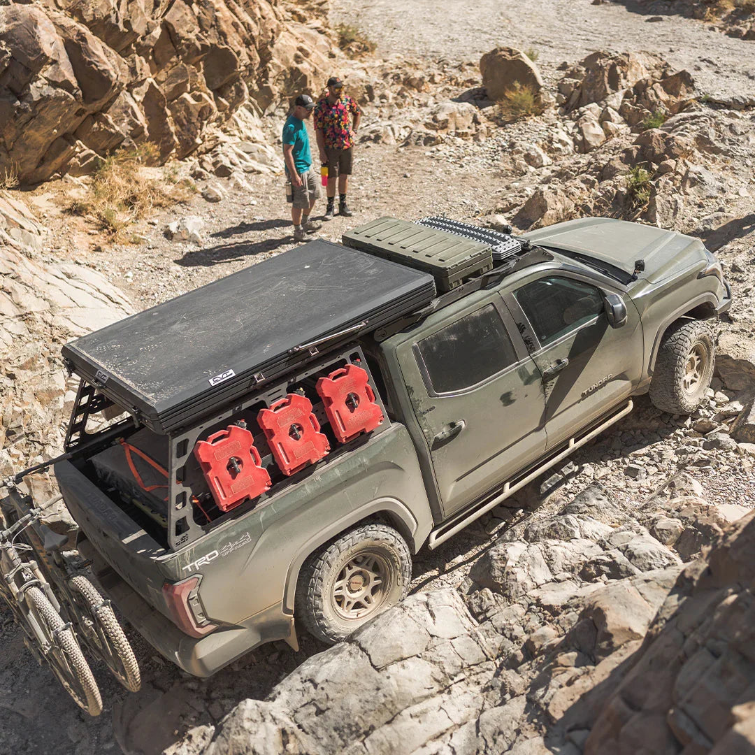 Toyota Tundra off-road with roof rack, red fuel cans, and camping gear in rocky desert terrain