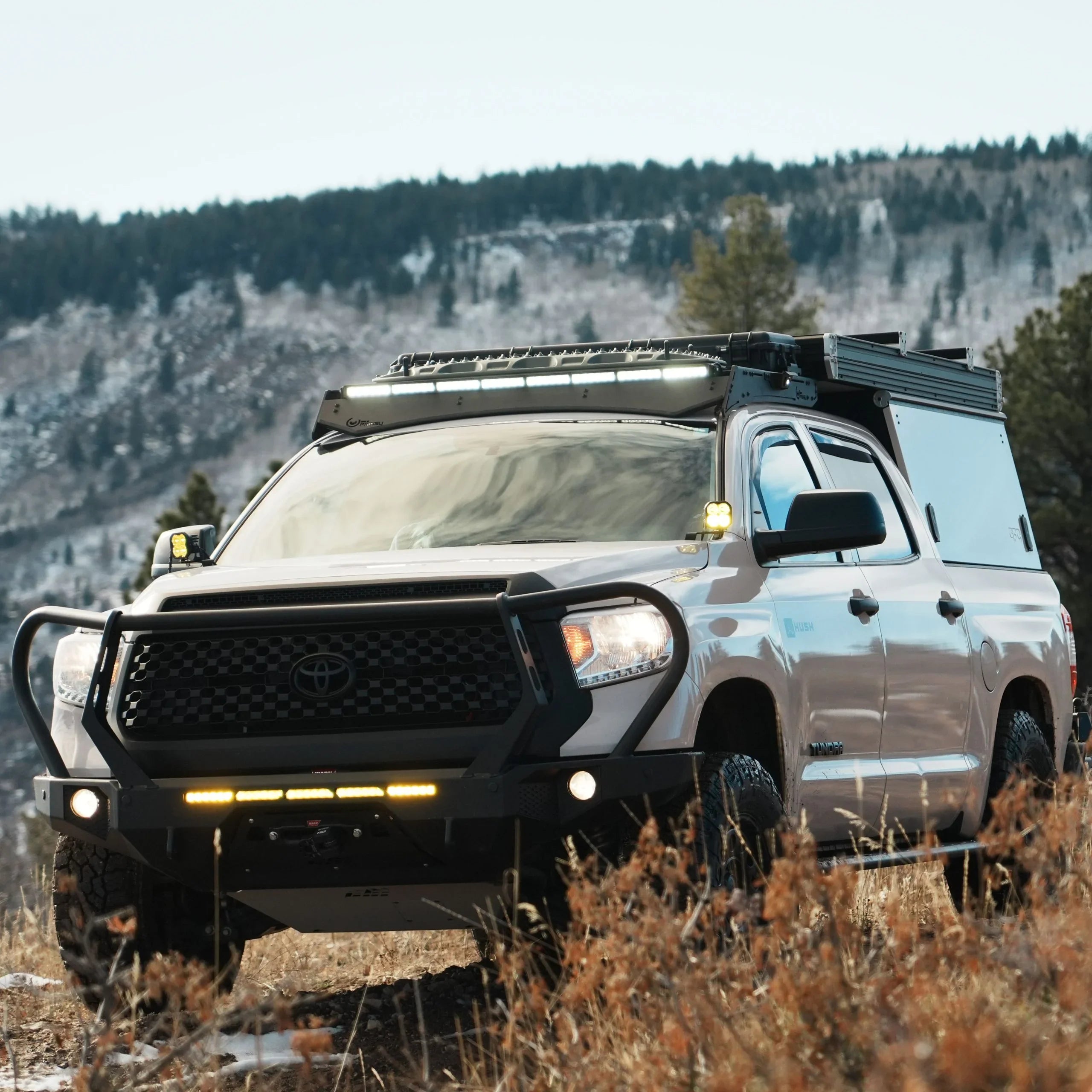 Toyota Tundra overland truck with roof rack, camper shell, and off-road accessories outdoors
