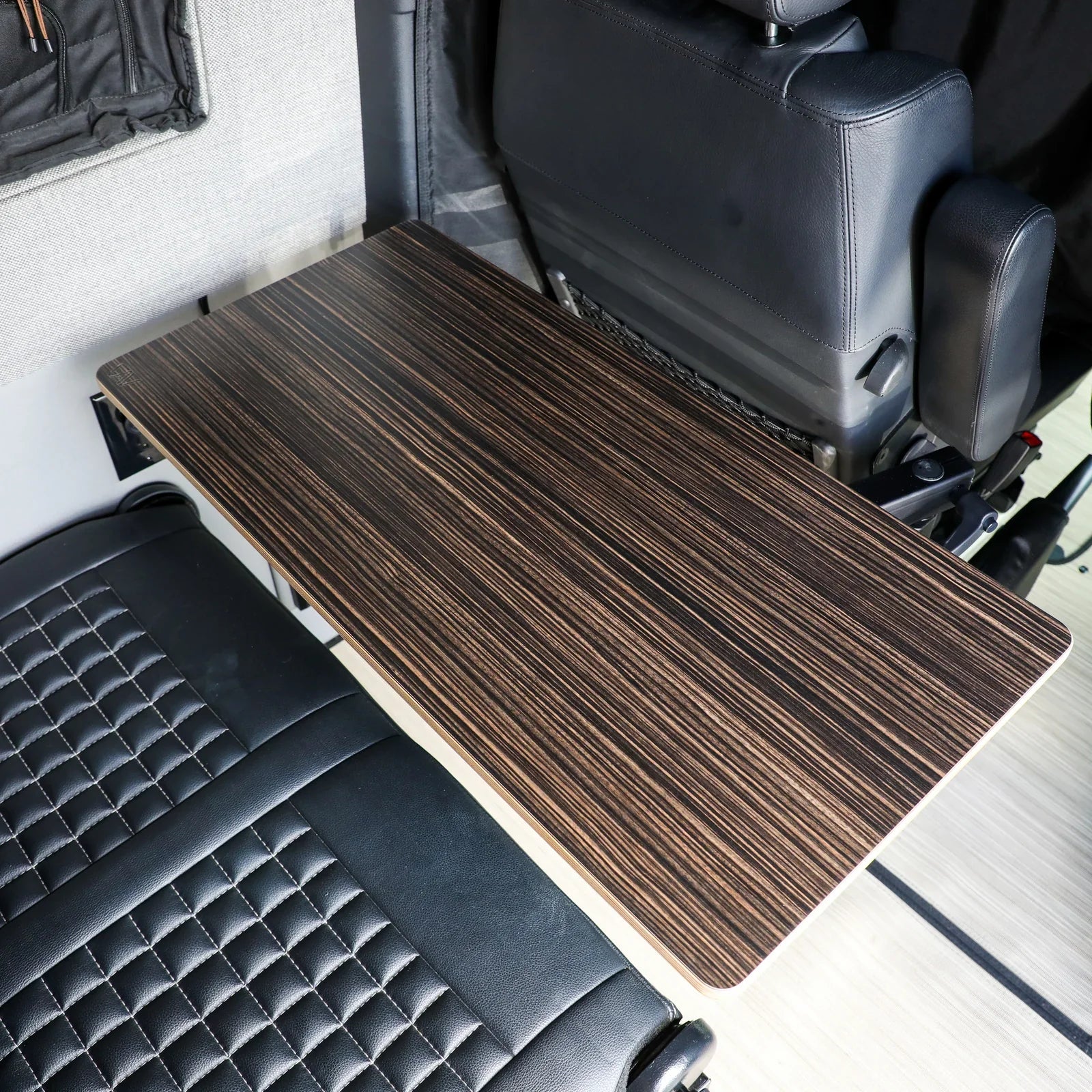 Ebony woodgrain vehicle camping table mounted between leather seats in an overlanding van