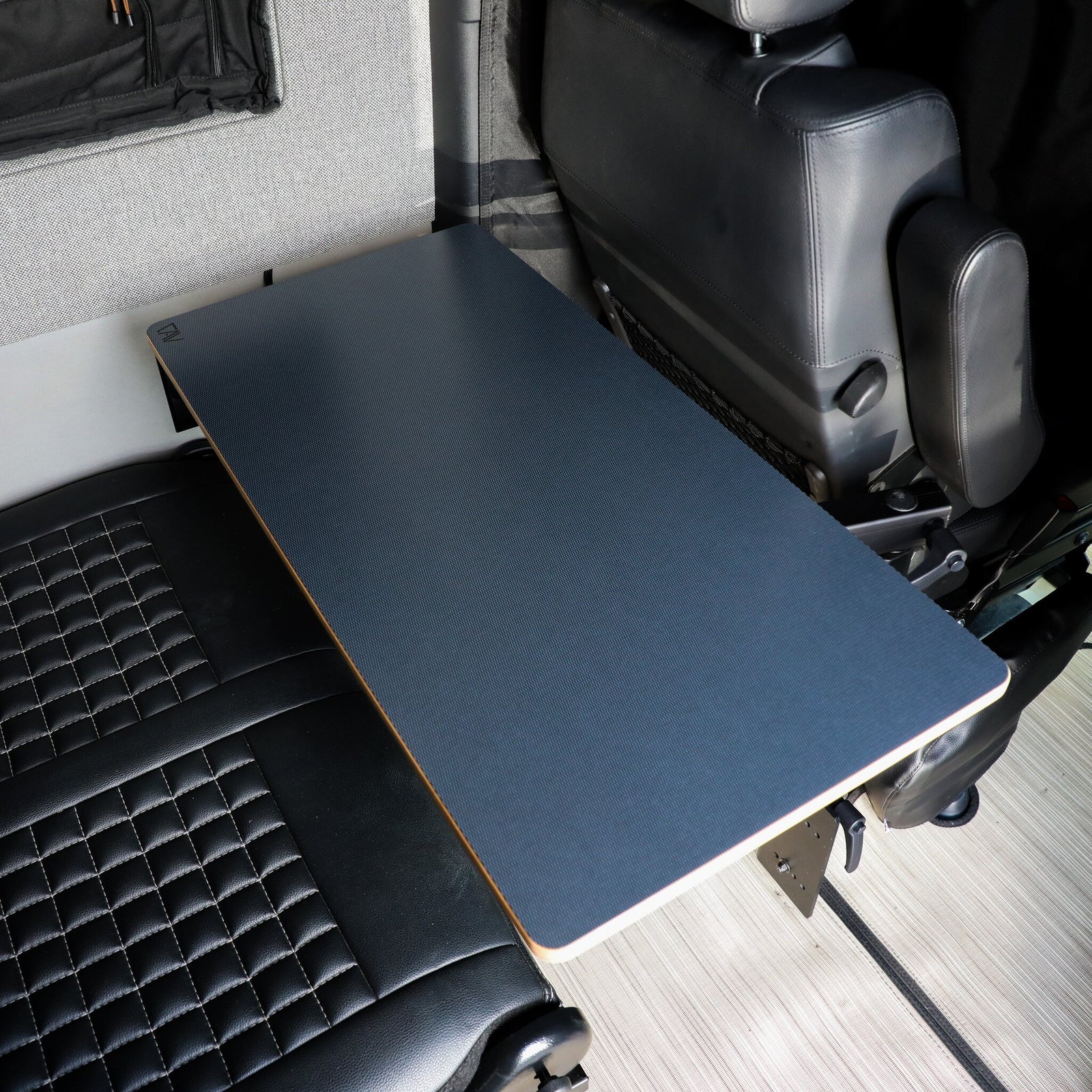 Folding navy blue campervan table mounted between leather seats and grey interior wall