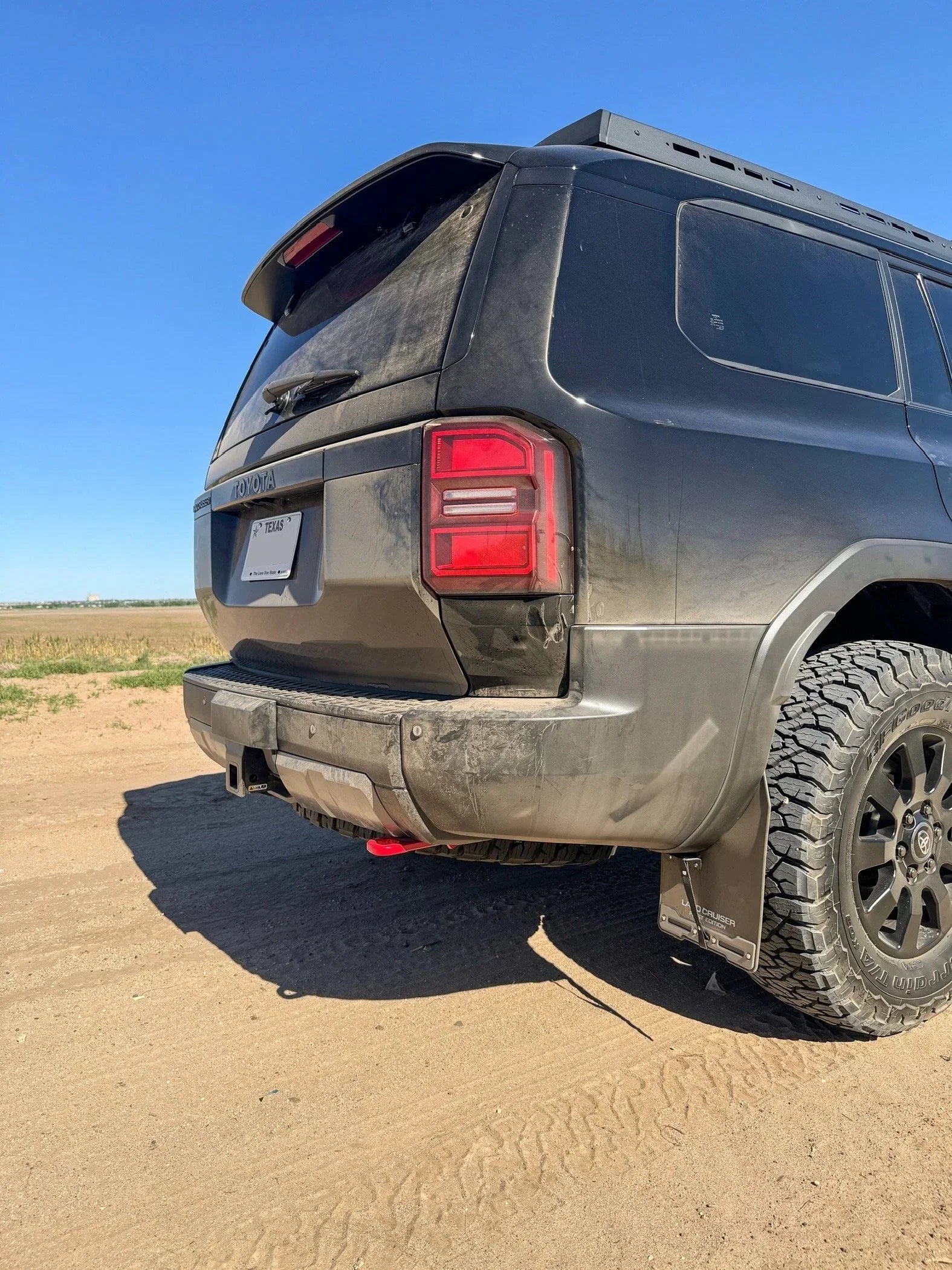 Rear view of dusty Toyota Land Cruiser SUV with off-road tires on a dirt road outdoors