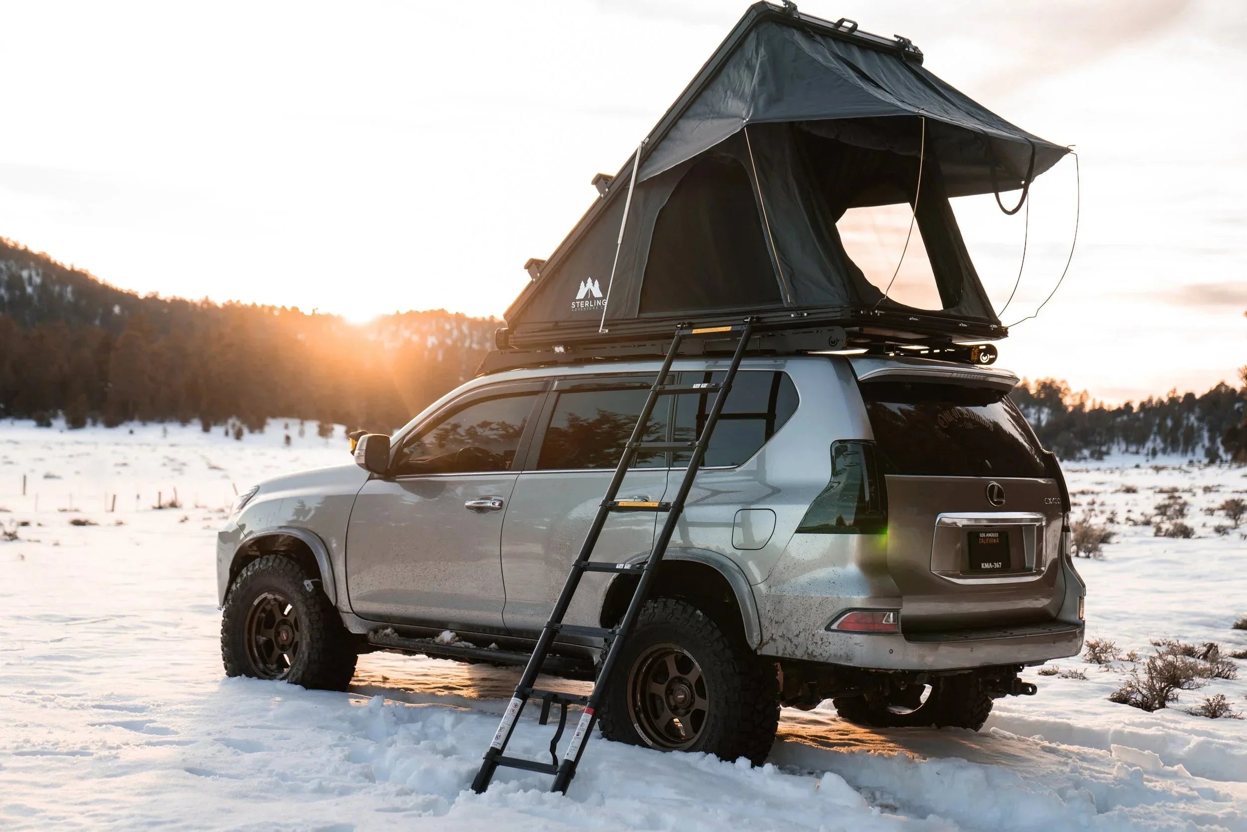 SUV with rooftop tent and ladder in snowy landscape at sunset, overlanding vehicle camping