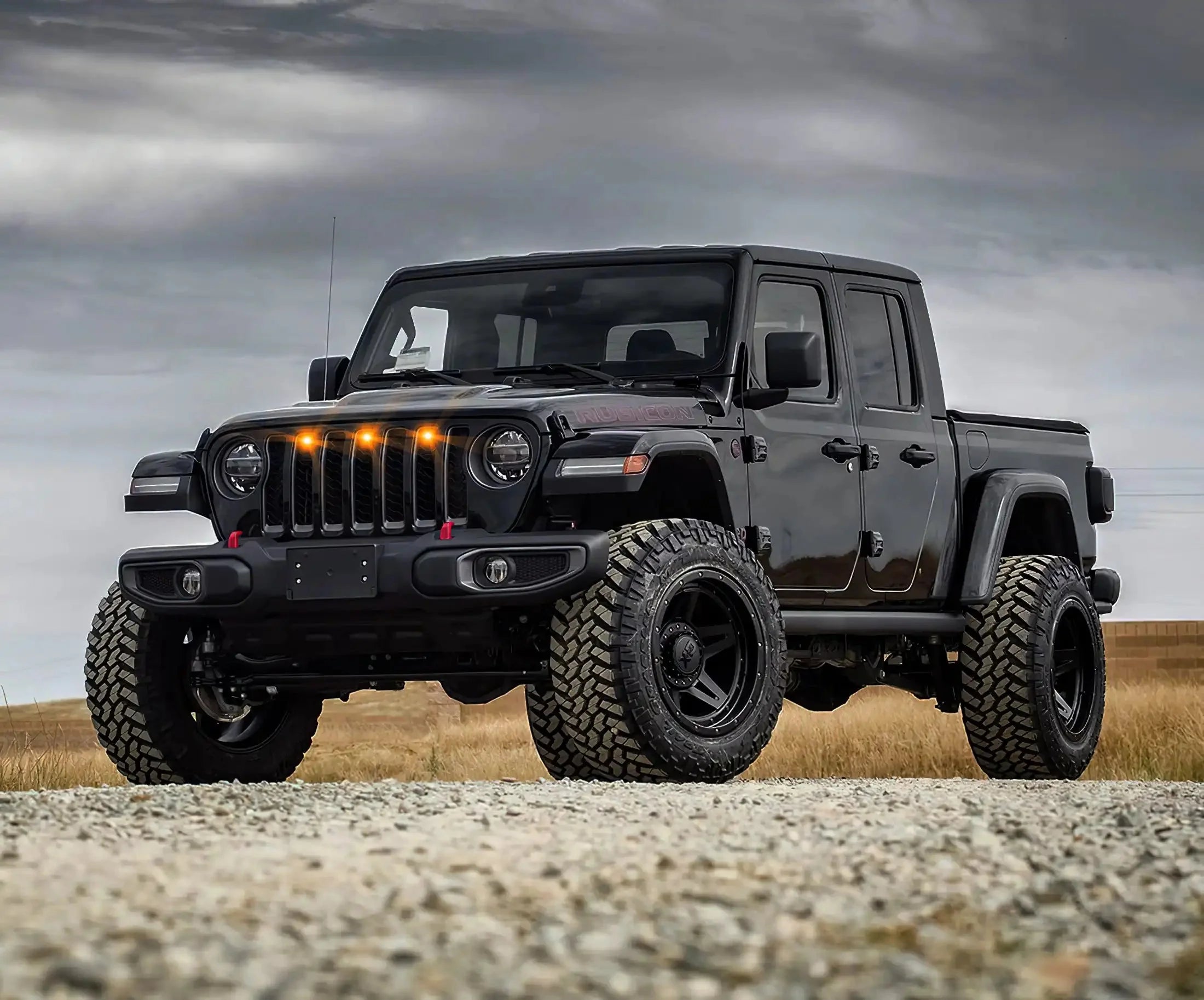 Lifted black Jeep Gladiator with off-road tires and amber grill lights on rocky trail