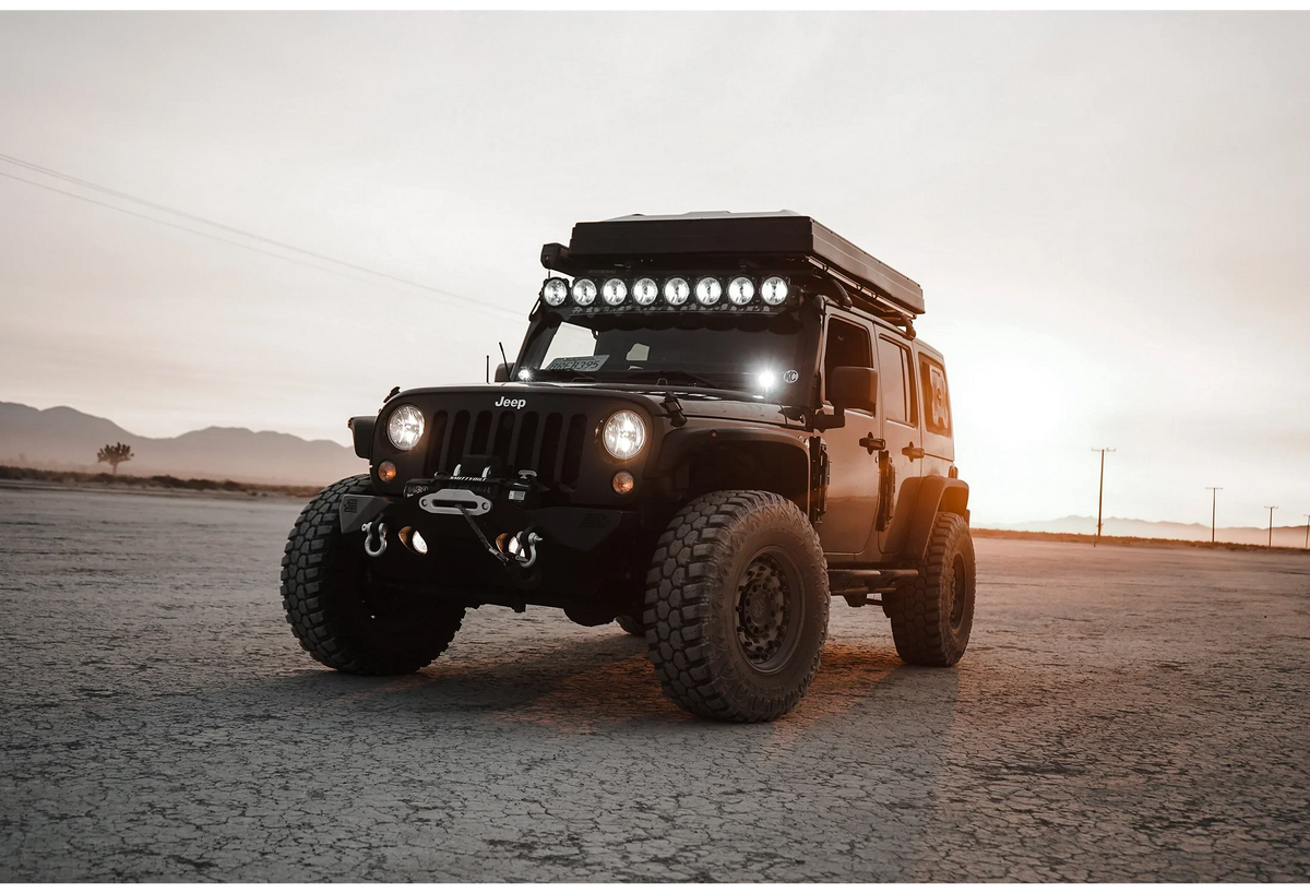 Black Jeep Wrangler 4x4 with off-road tires, roof rack, and light bar in a desert setting