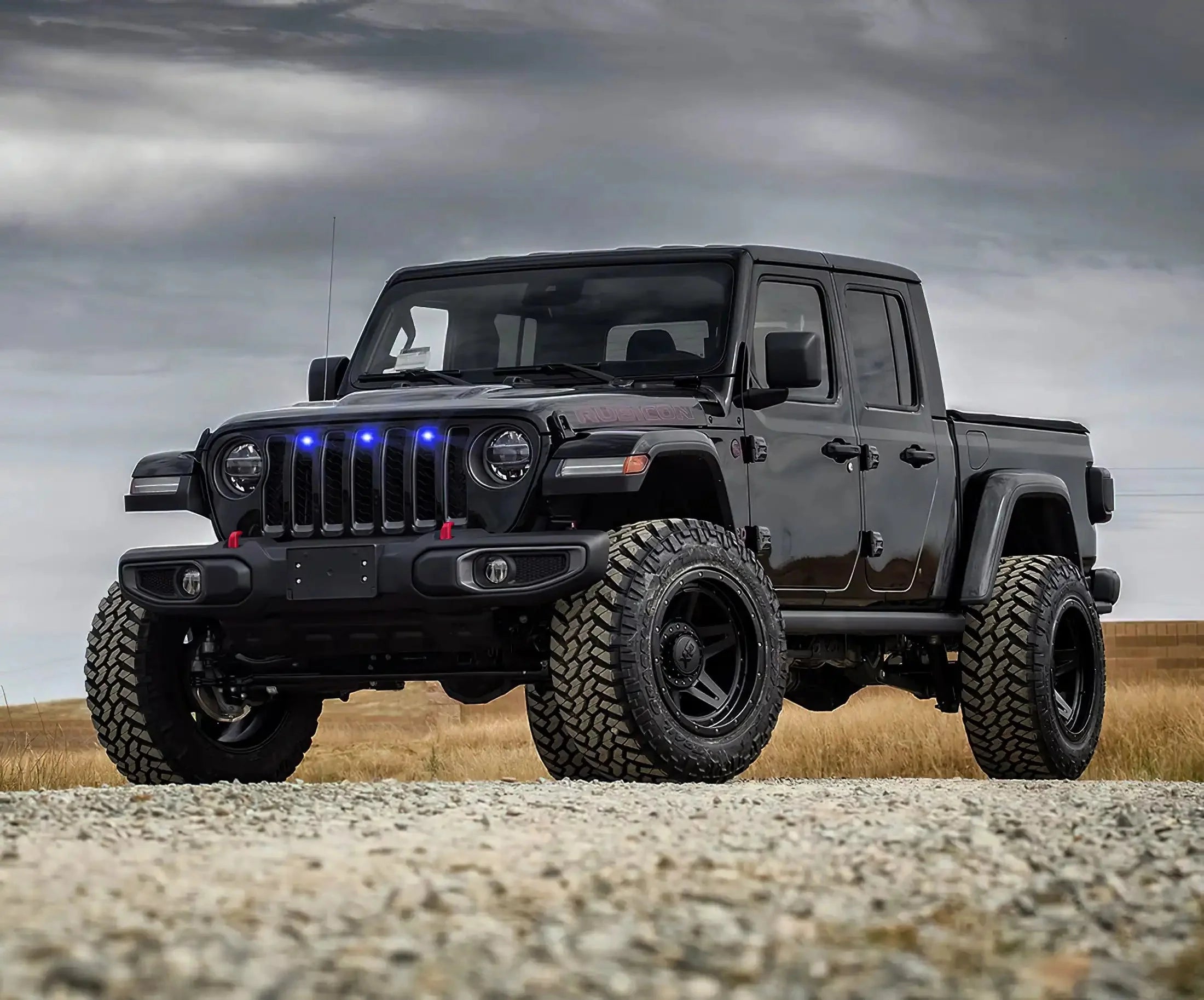 Black Jeep Gladiator with off-road tires, lifted suspension, and blue grille lights outdoors