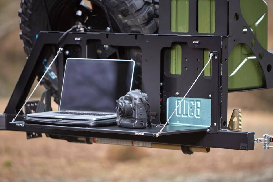 Offroad camp table mounted on vehicle bumper with laptop and camera outdoors