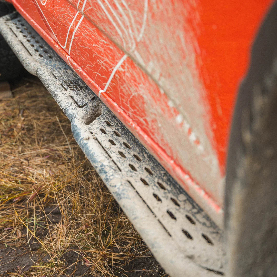 Close-up of rugged rock slider on dirty red off-road vehicle, side view, outdoor setting