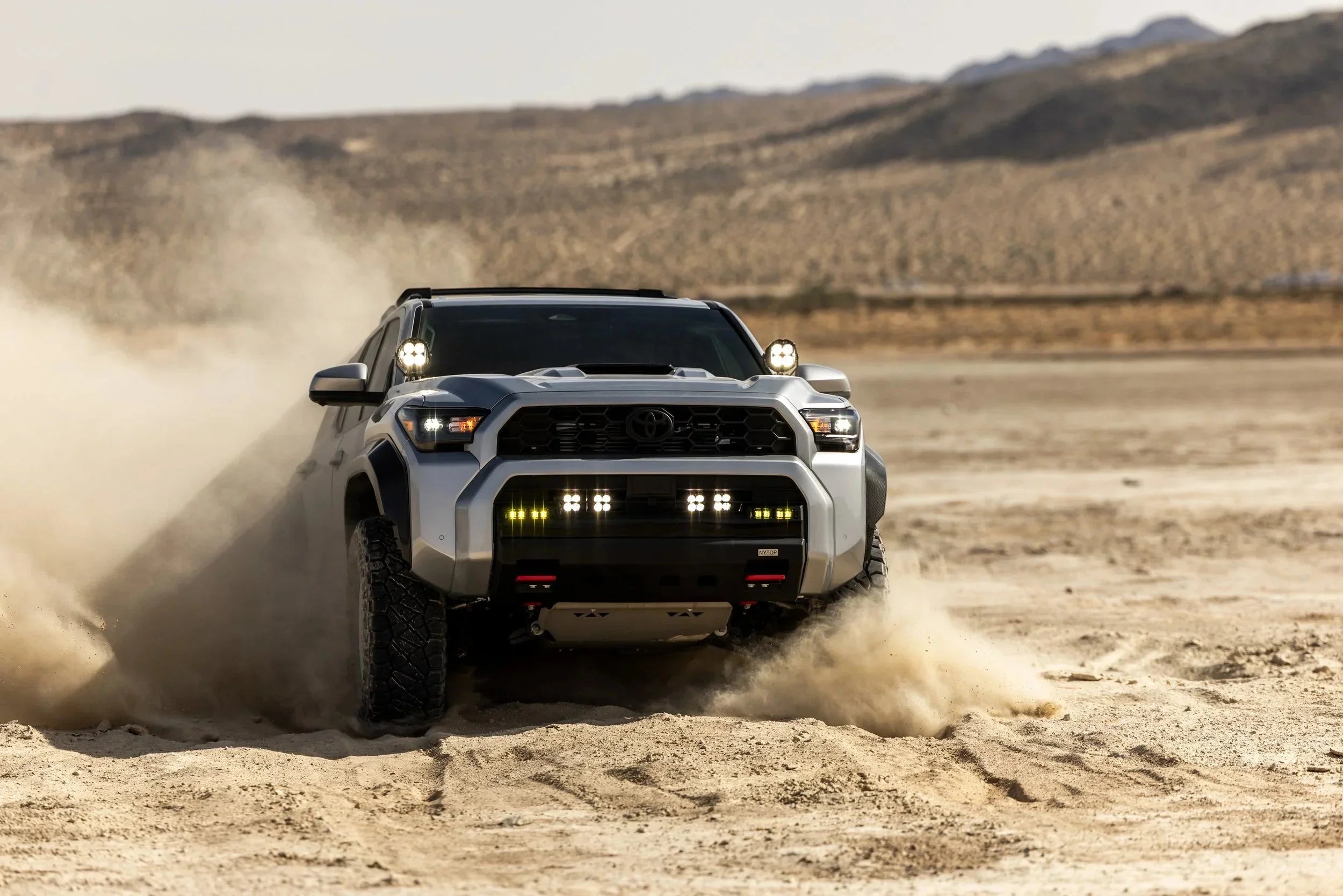 Toyota Tacoma off-road truck driving through desert sand with bright LED lights