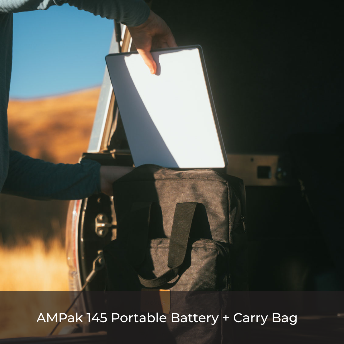 Person placing portable battery into black carry bag near vehicle with outdoor background