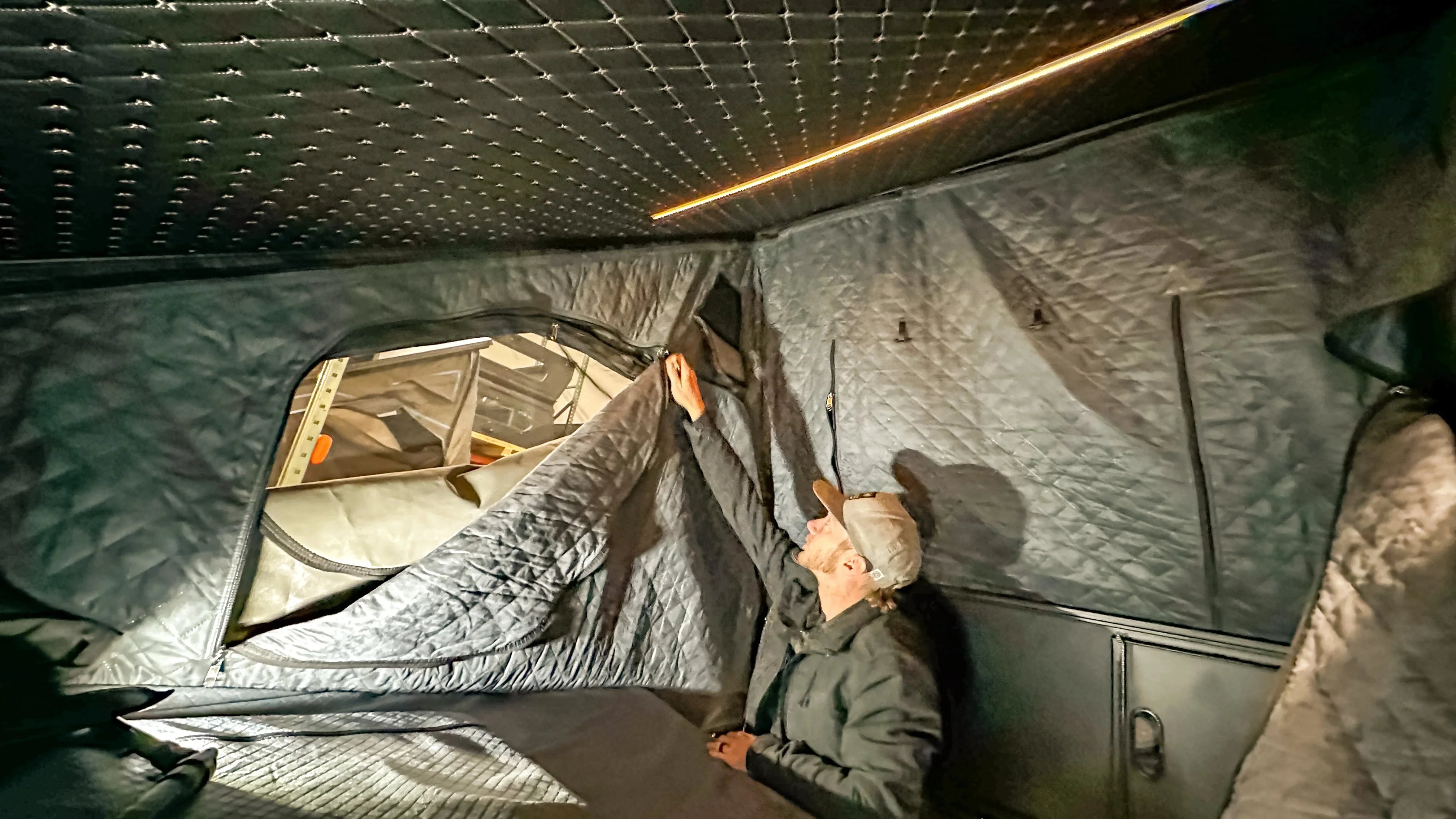 Man installs quilted camper insulation for winterizing overland vehicle interior.