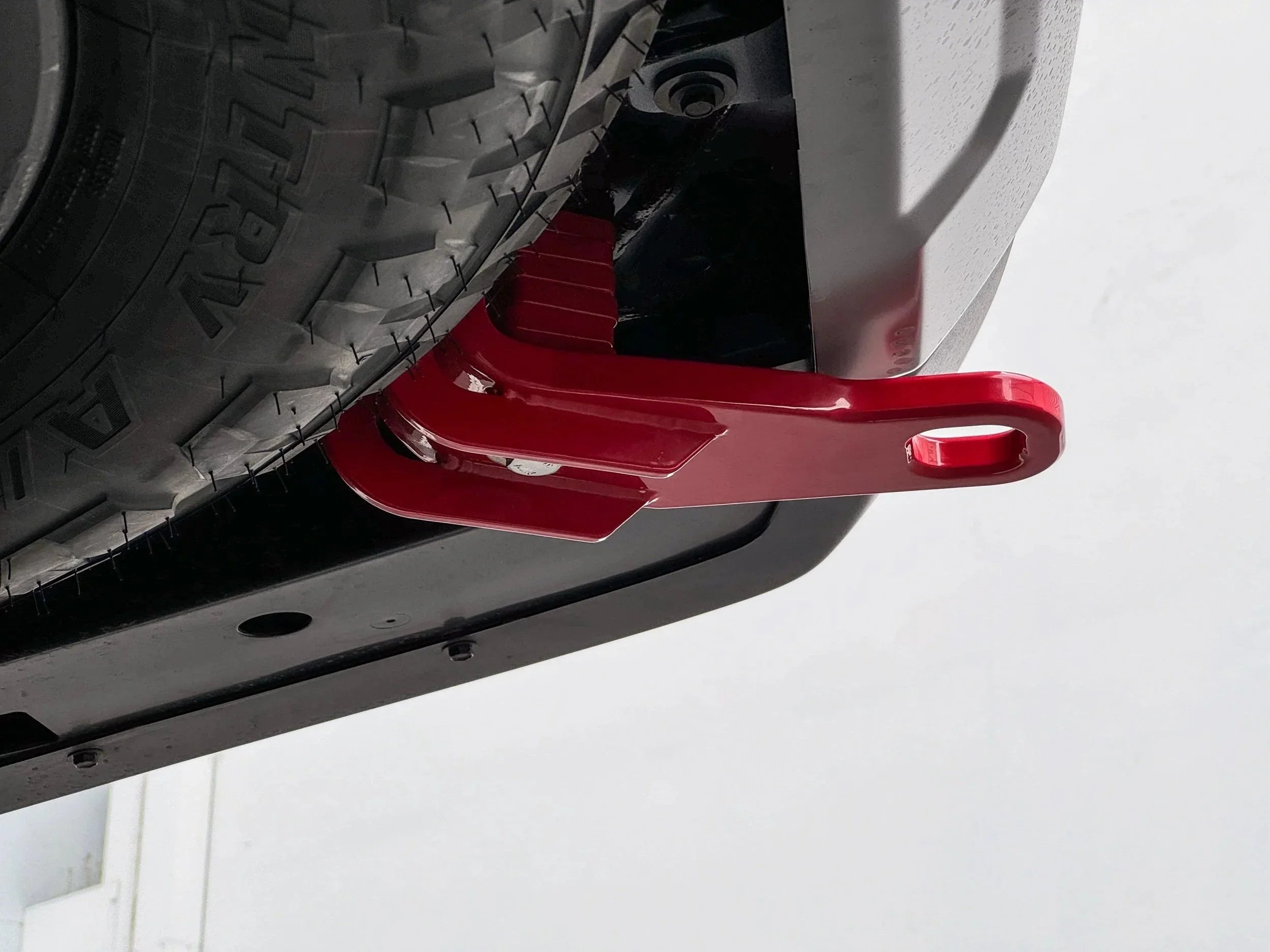 Red rear recovery point mounted on vehicle undercarriage near all-terrain tire