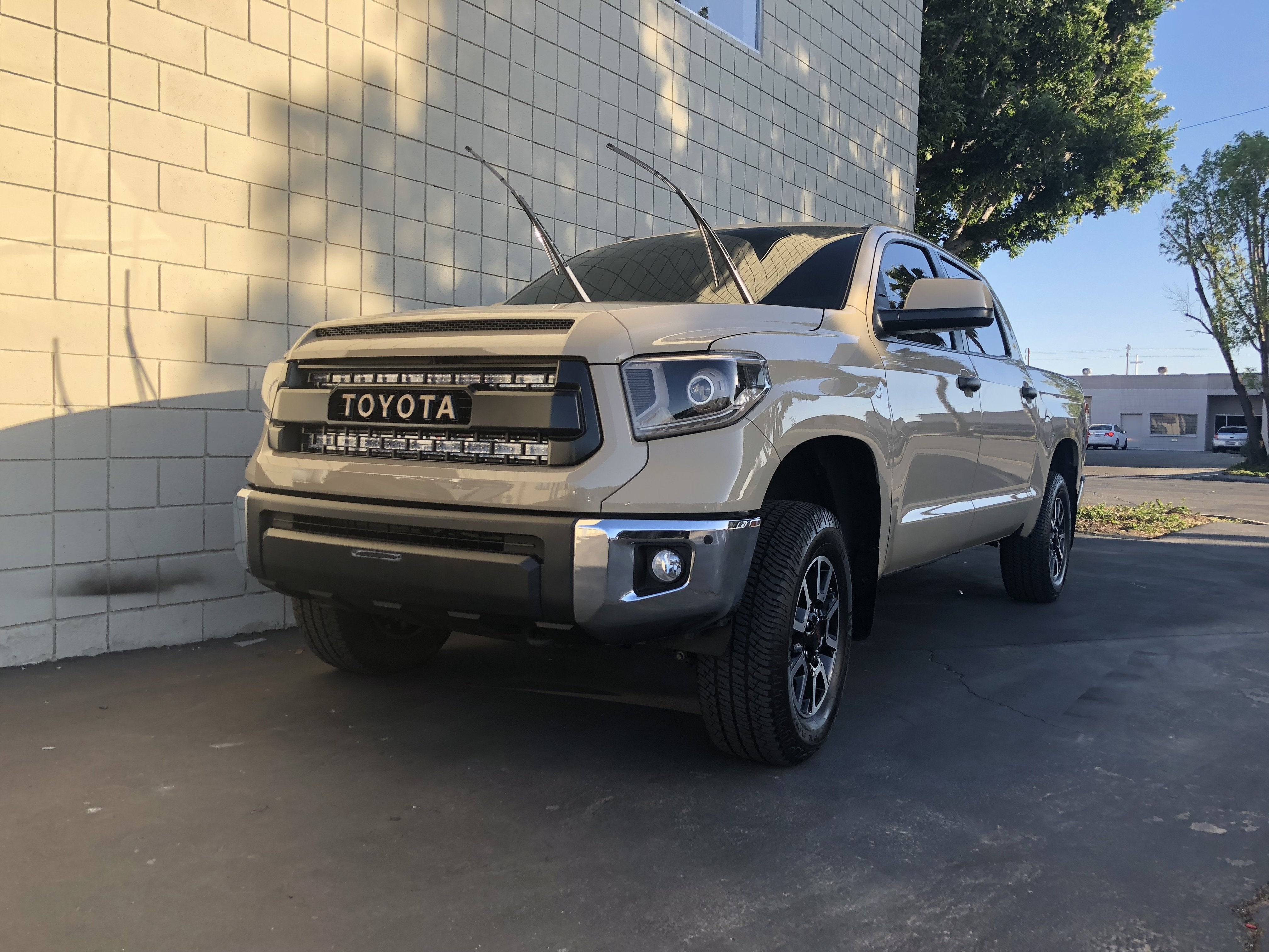 Beige Toyota Tundra pickup truck with aftermarket grille parked outside against a brick wall