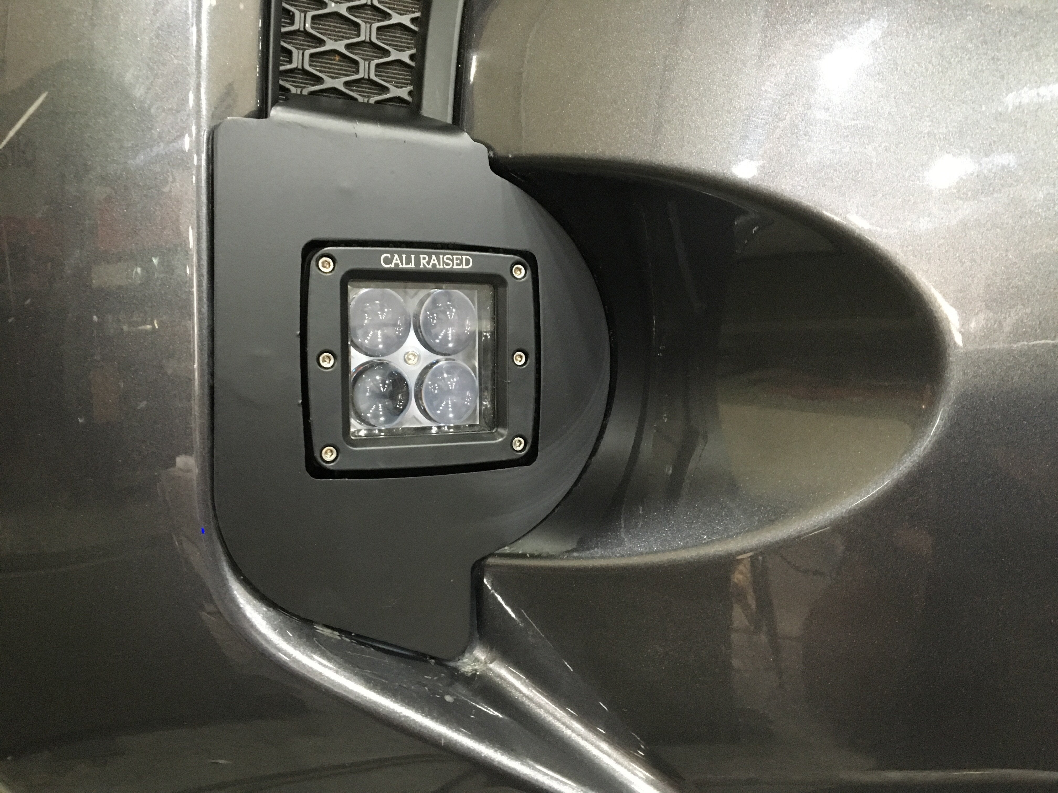 Cali Raised LED fog light pod installed on a vehicle front bumper, close-up view