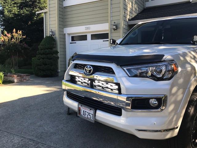 White Toyota 4Runner SUV with aftermarket grille lights parked in a residential driveway