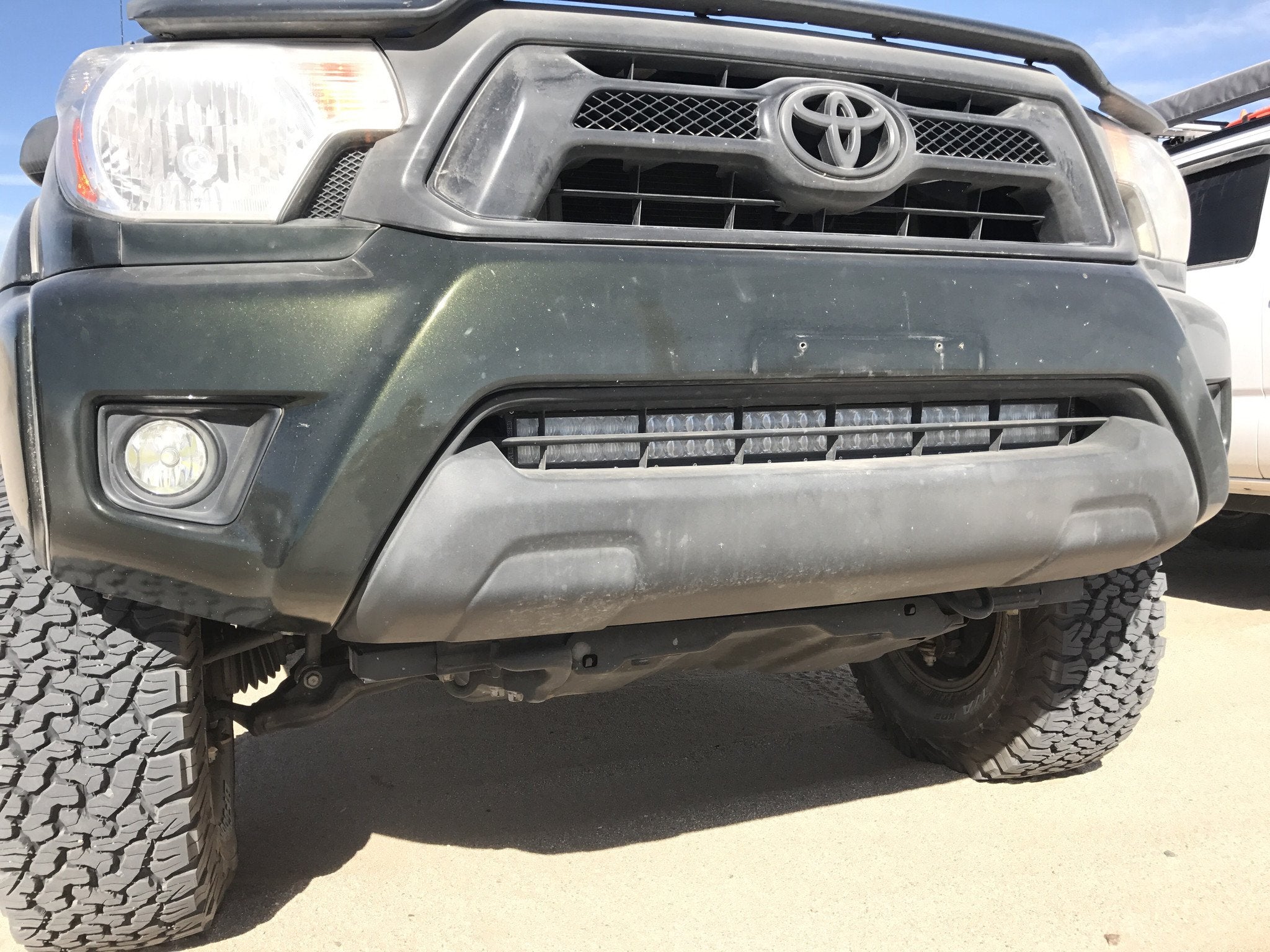 Toyota Tacoma front bumper with off-road LED light bar and rugged tires, outdoor setting