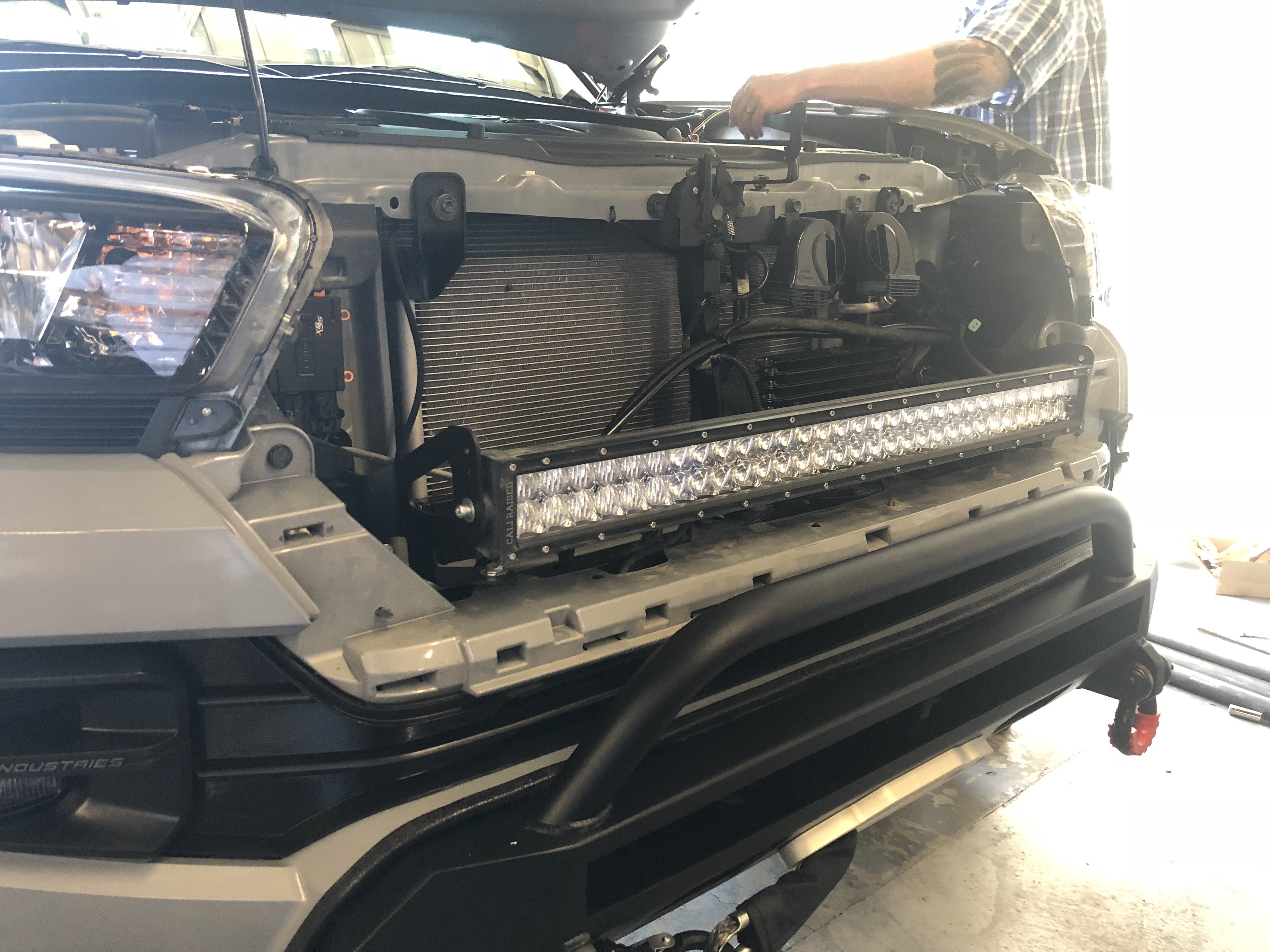 Front grille removed from off-road vehicle showing LED light bar installation