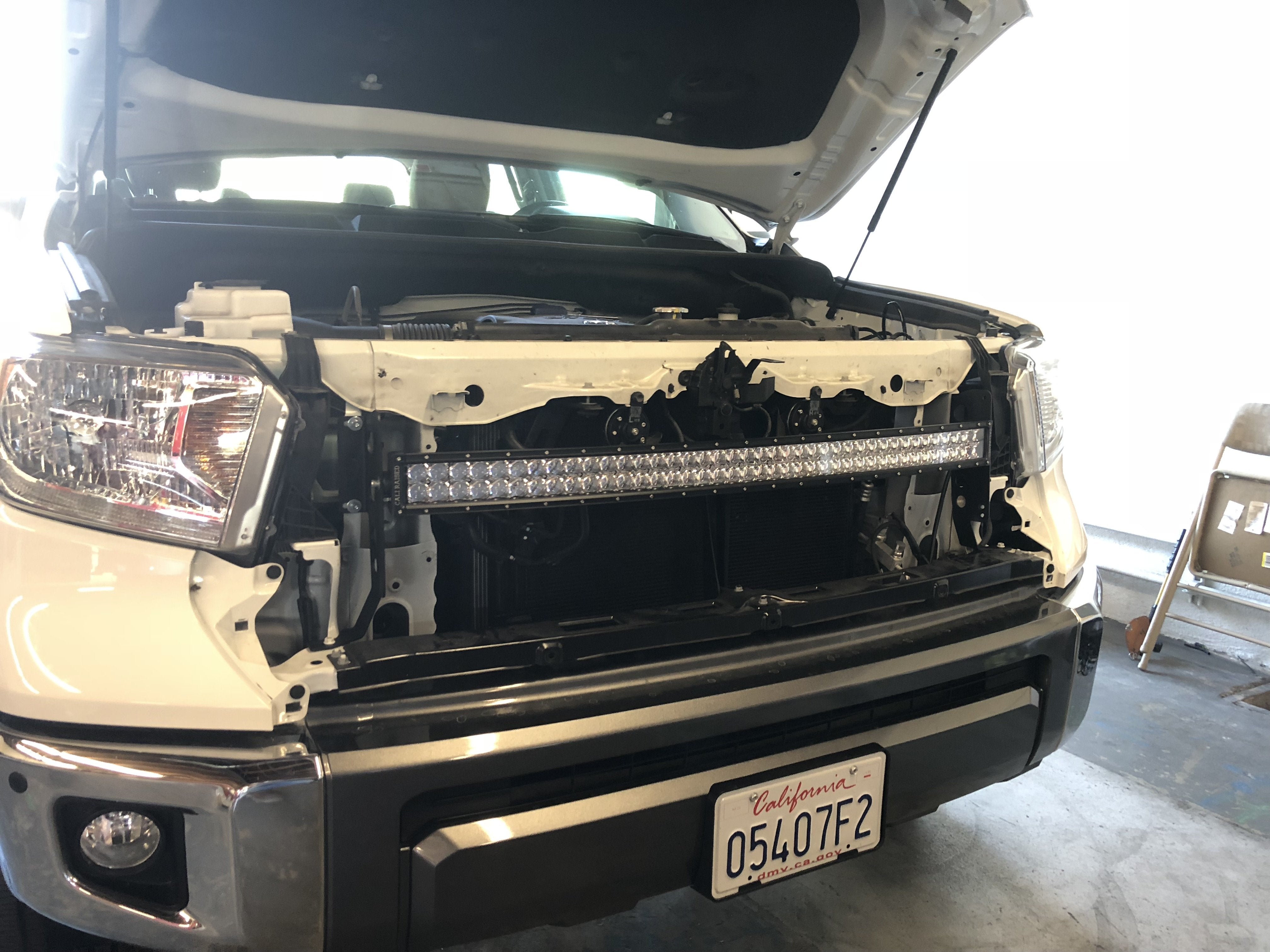 Toyota truck with grille removed, showing front LED light bar installation for off-road use