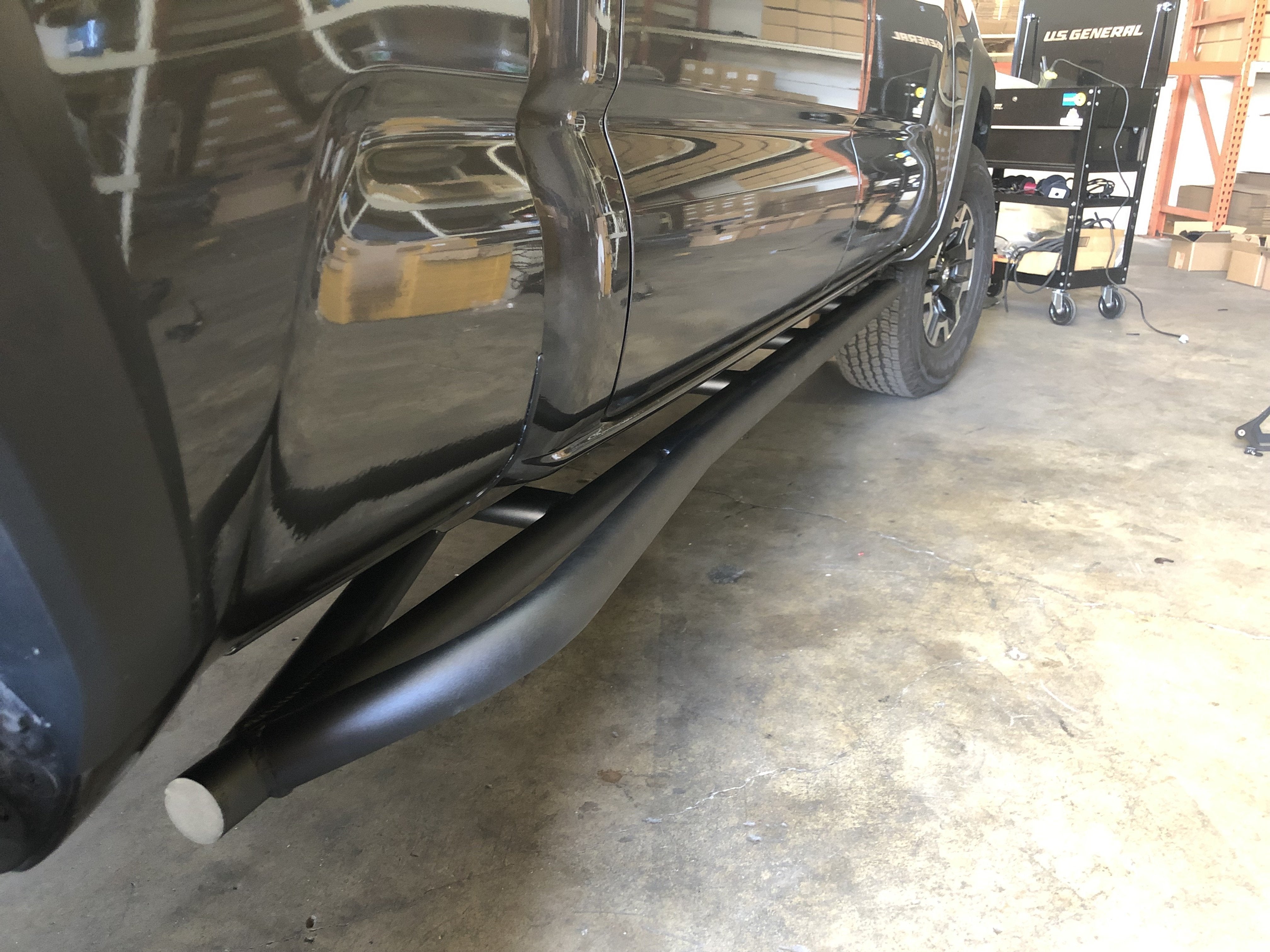 Black off-road rock sliders installed on a Toyota Tacoma in a garage setting