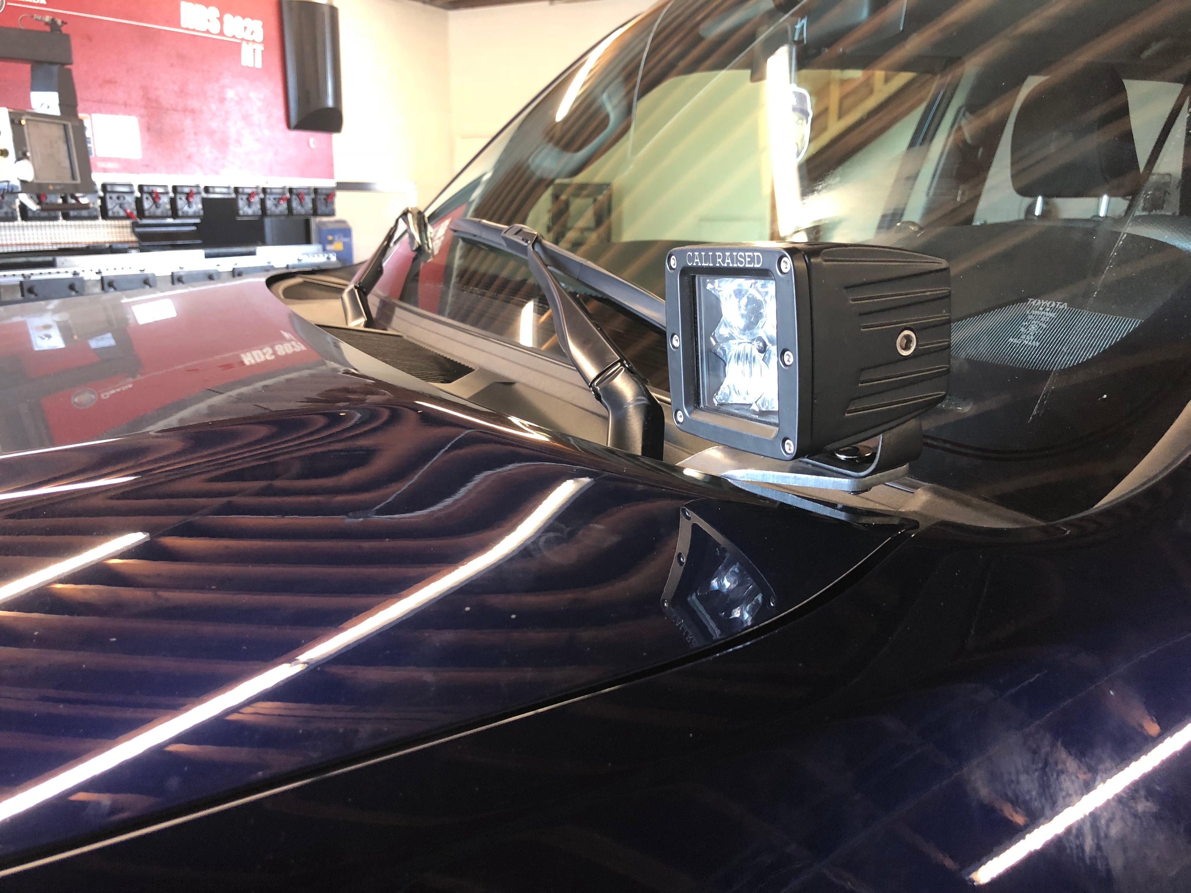 Off-road LED ditch light mounted near windshield on a dark SUV or truck in garage