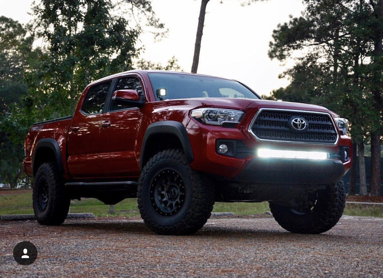 Red Toyota Tacoma with off-road tires and front LED light bar parked outdoors