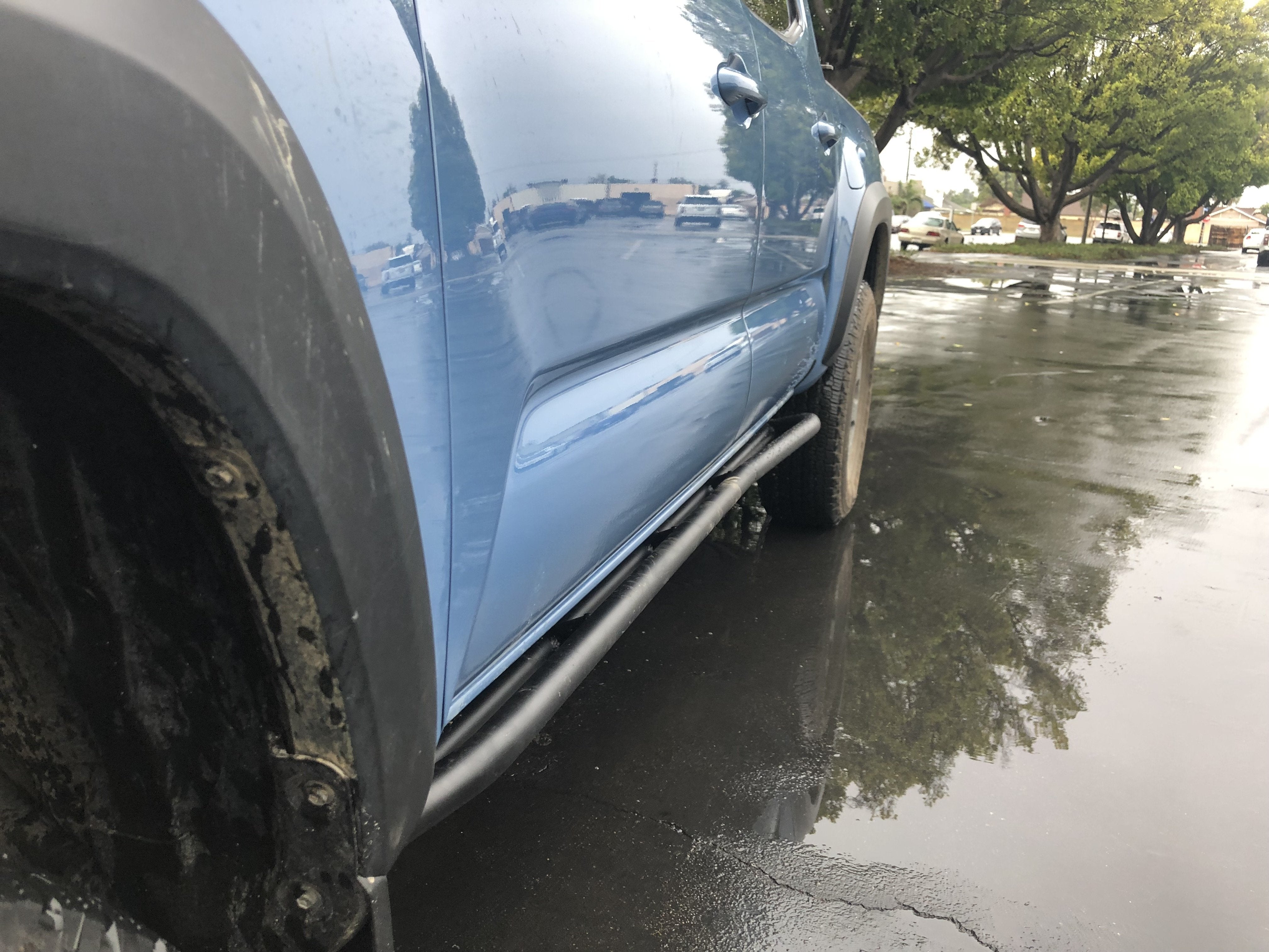 Close-up of blue Toyota Tacoma with off-road rock sliders in wet parking lot