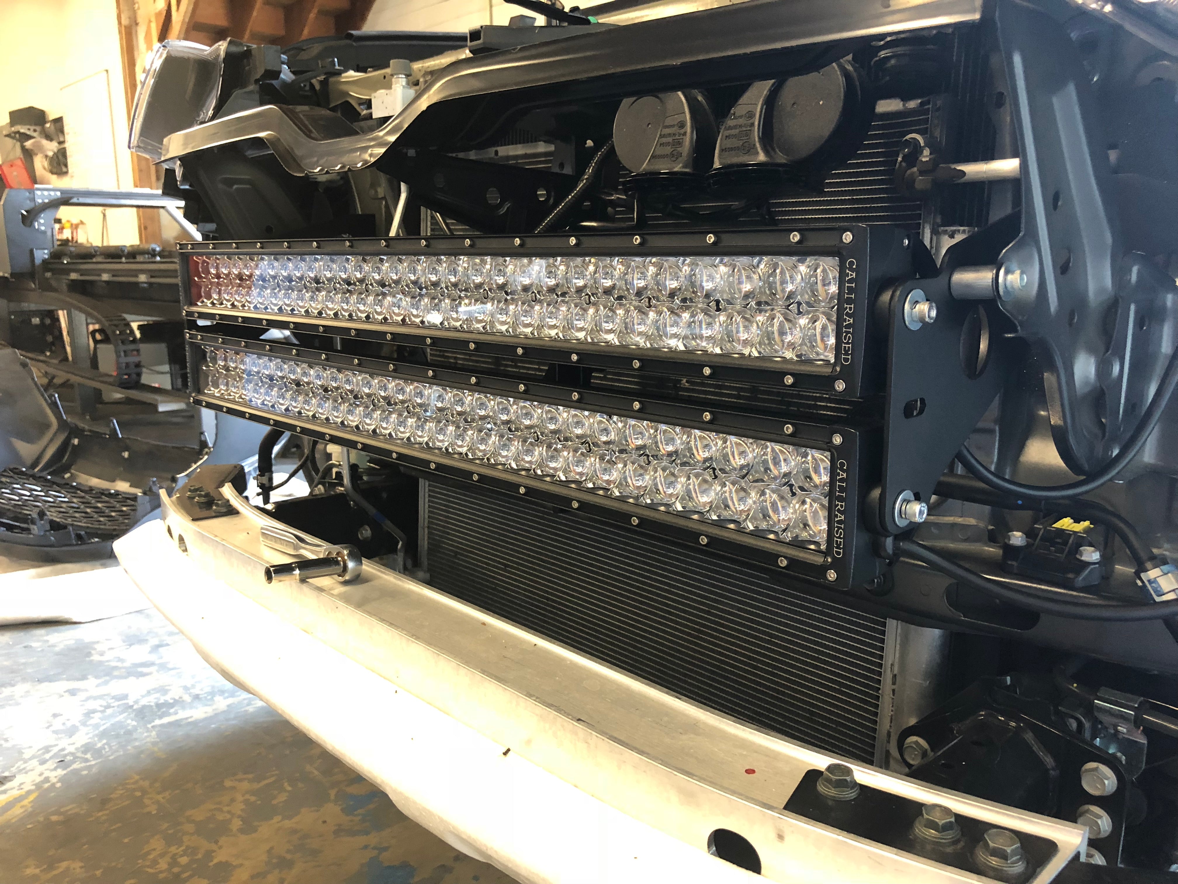 Dual off-road LED light bars installed on front grille of a vehicle in a garage setting.