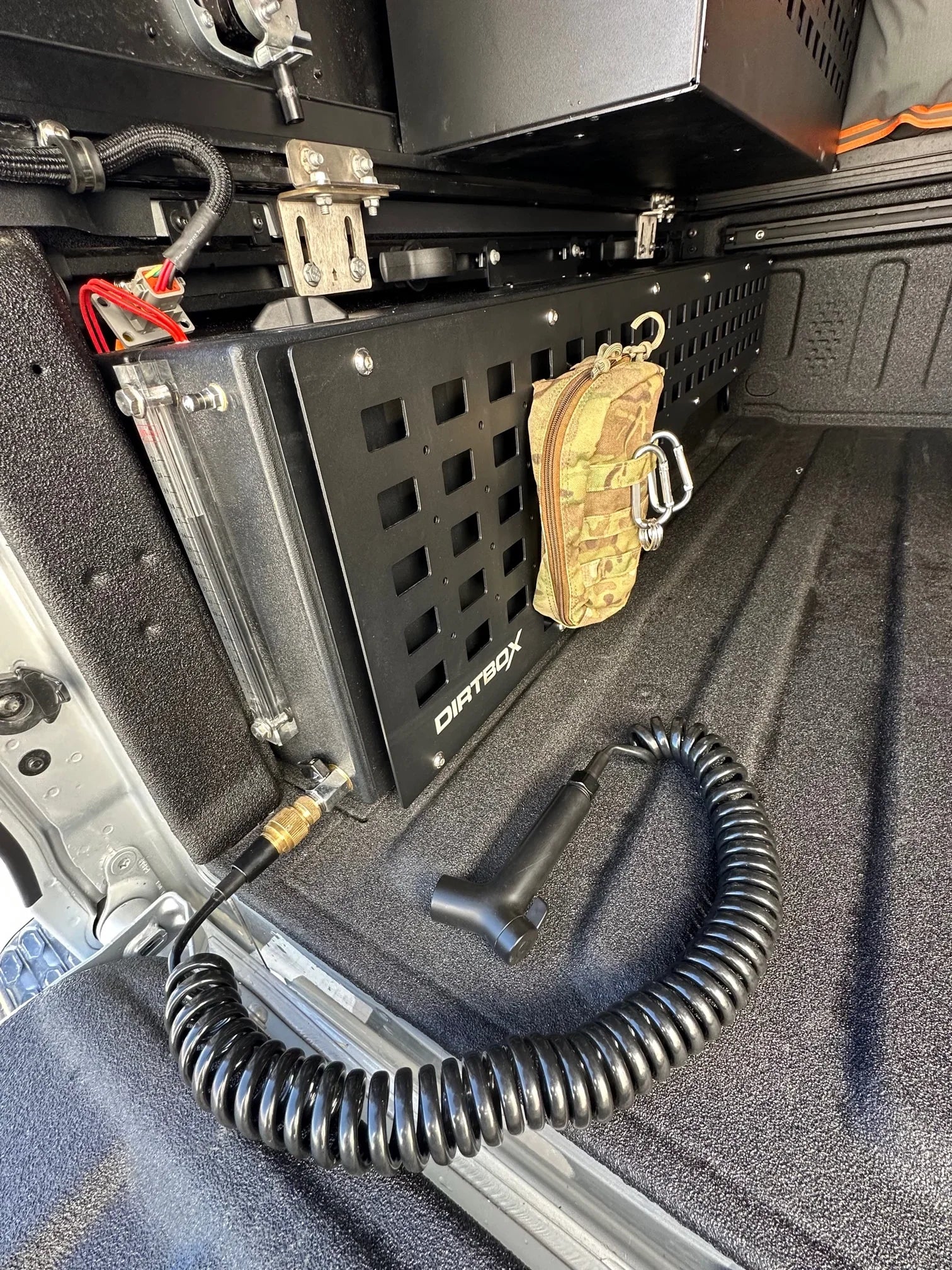 In-bed water tank system with mounted storage panel and coiled hose for overlanding vehicles