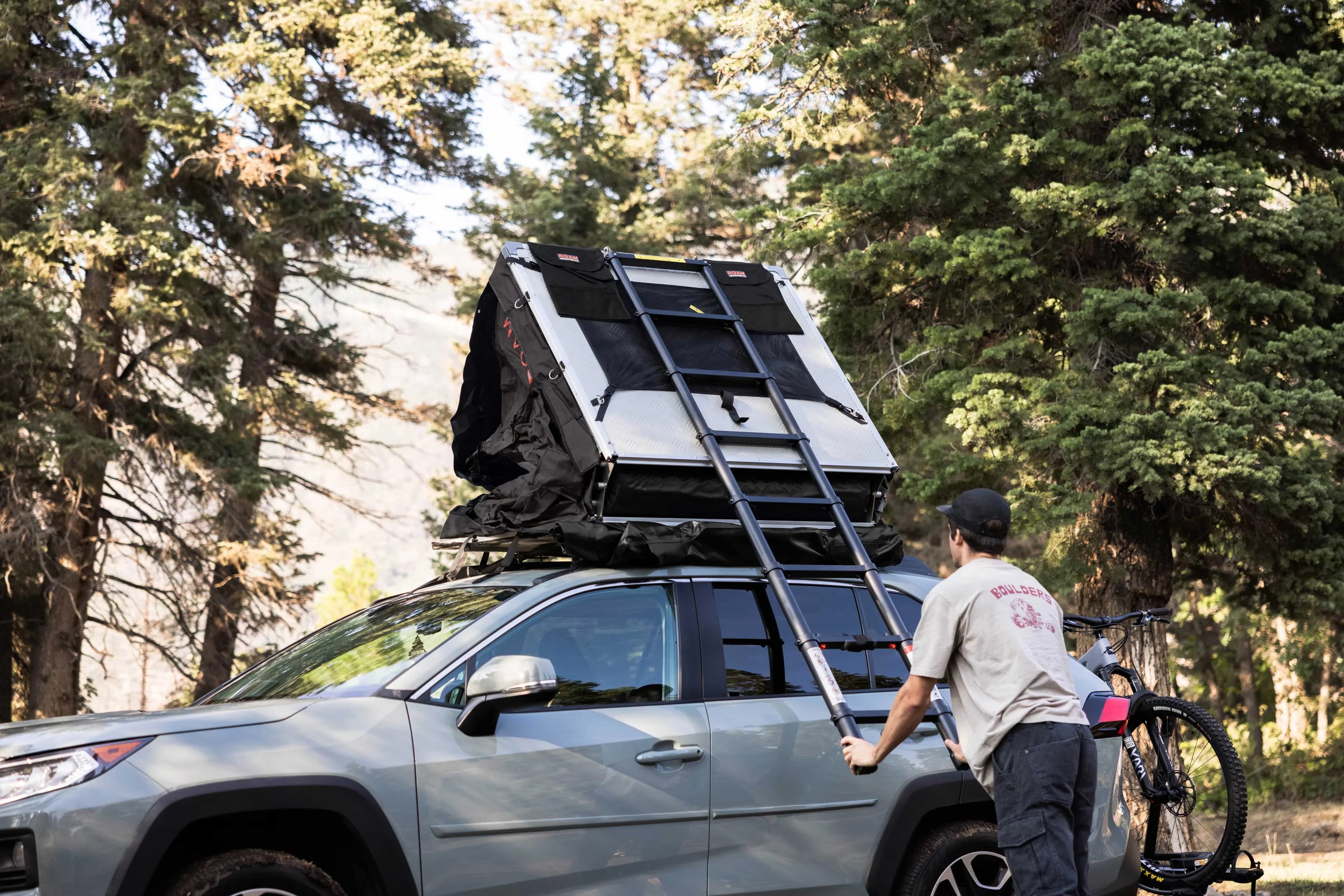 SUV with rooftop tent and bike rack in forest, overlanding camping gear setup