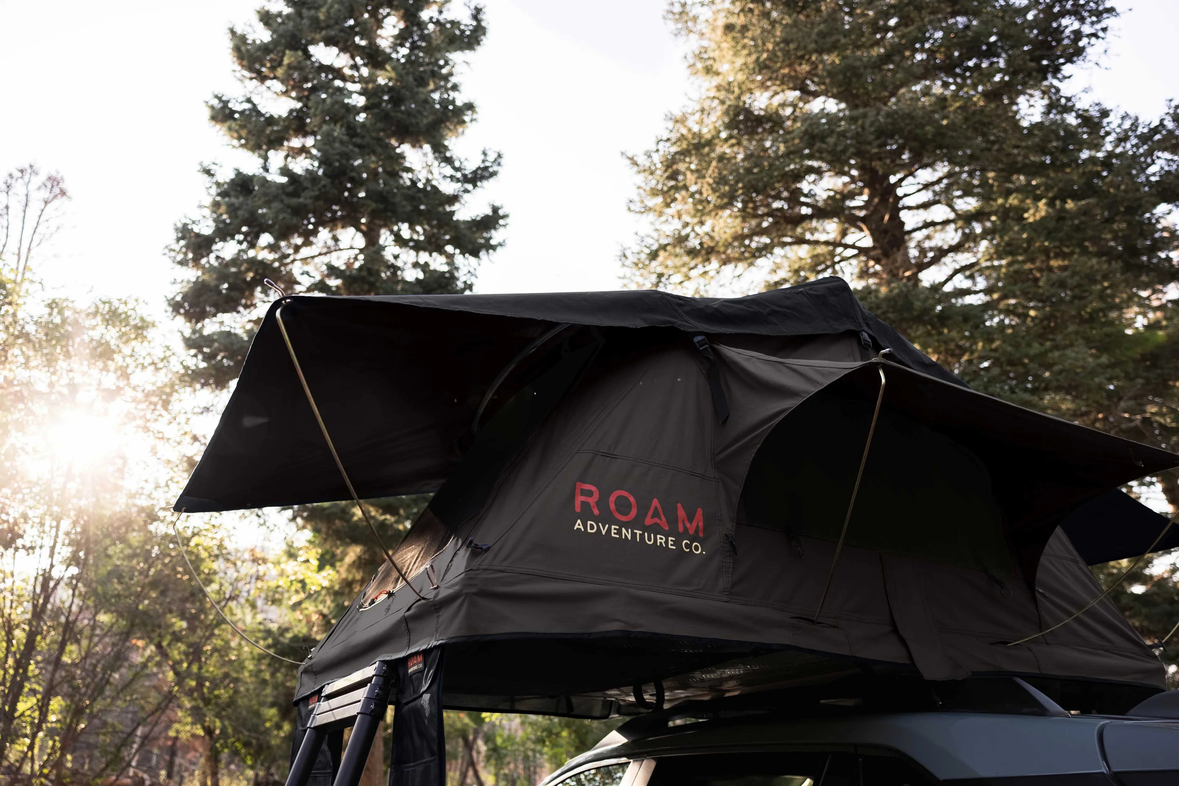 ROAM rooftop tent set up on vehicle for overlanding camping in pine forest at sunset